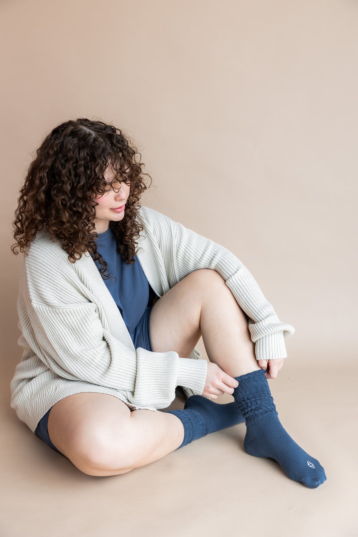 Model sitting on a beige background wearing Women’s Biker Short Set in Oxford with Adult Socks in Oxford and Oversized Chunky Knit Cardigan