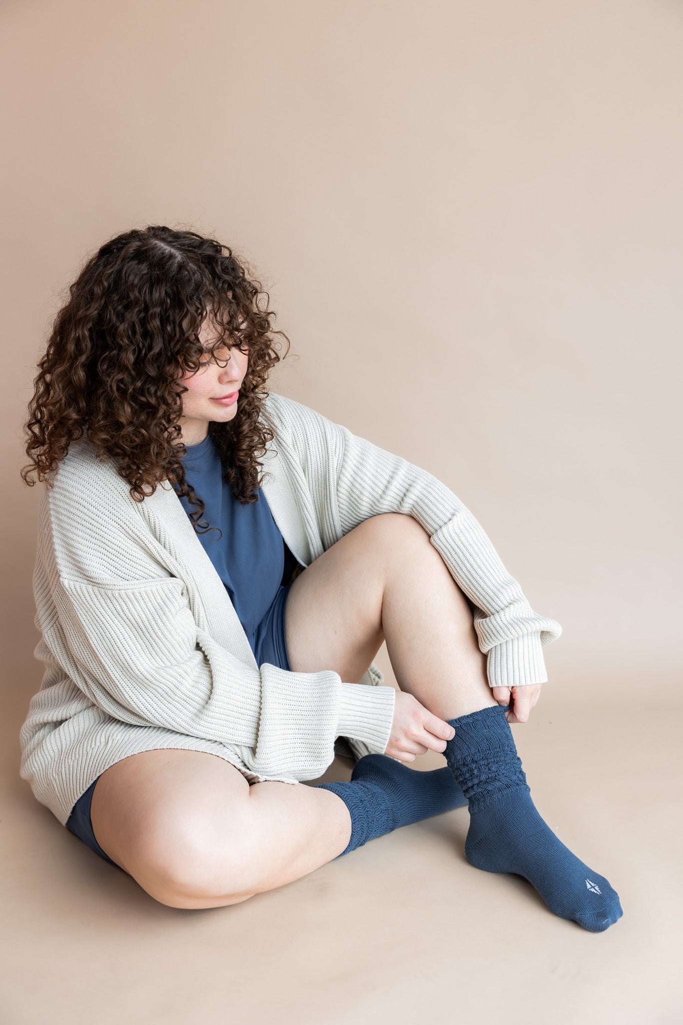 Model sitting on a beige background wearing Women’s Biker Short Set in Oxford with Adult Socks in Oxford and Oversized Chunky Knit Cardigan