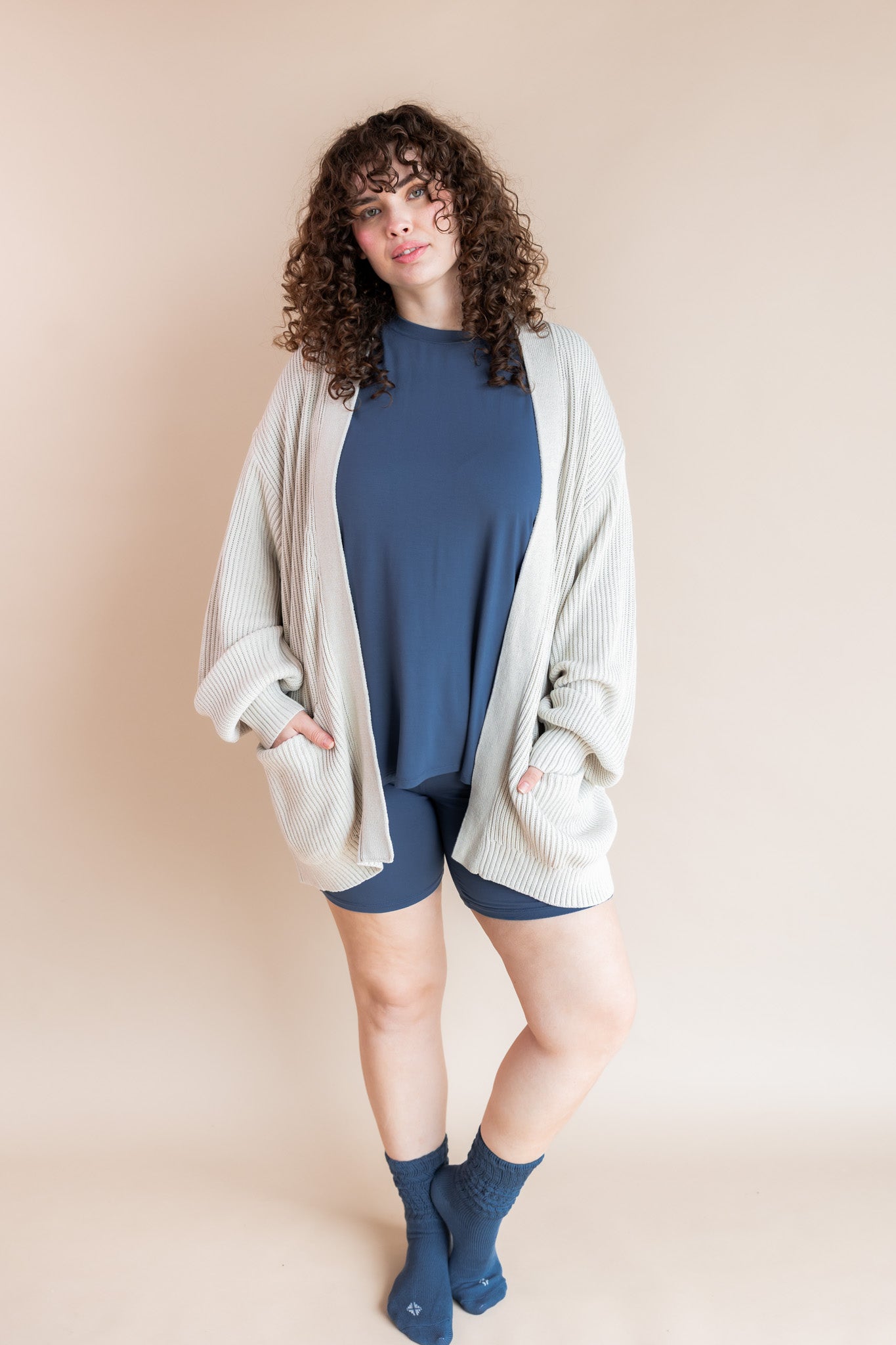 Model wearing Women’s Biker Short Set in Oxford with Adult Socks in Oxford and Oversized Chunky Knit Cardigan on a beige background