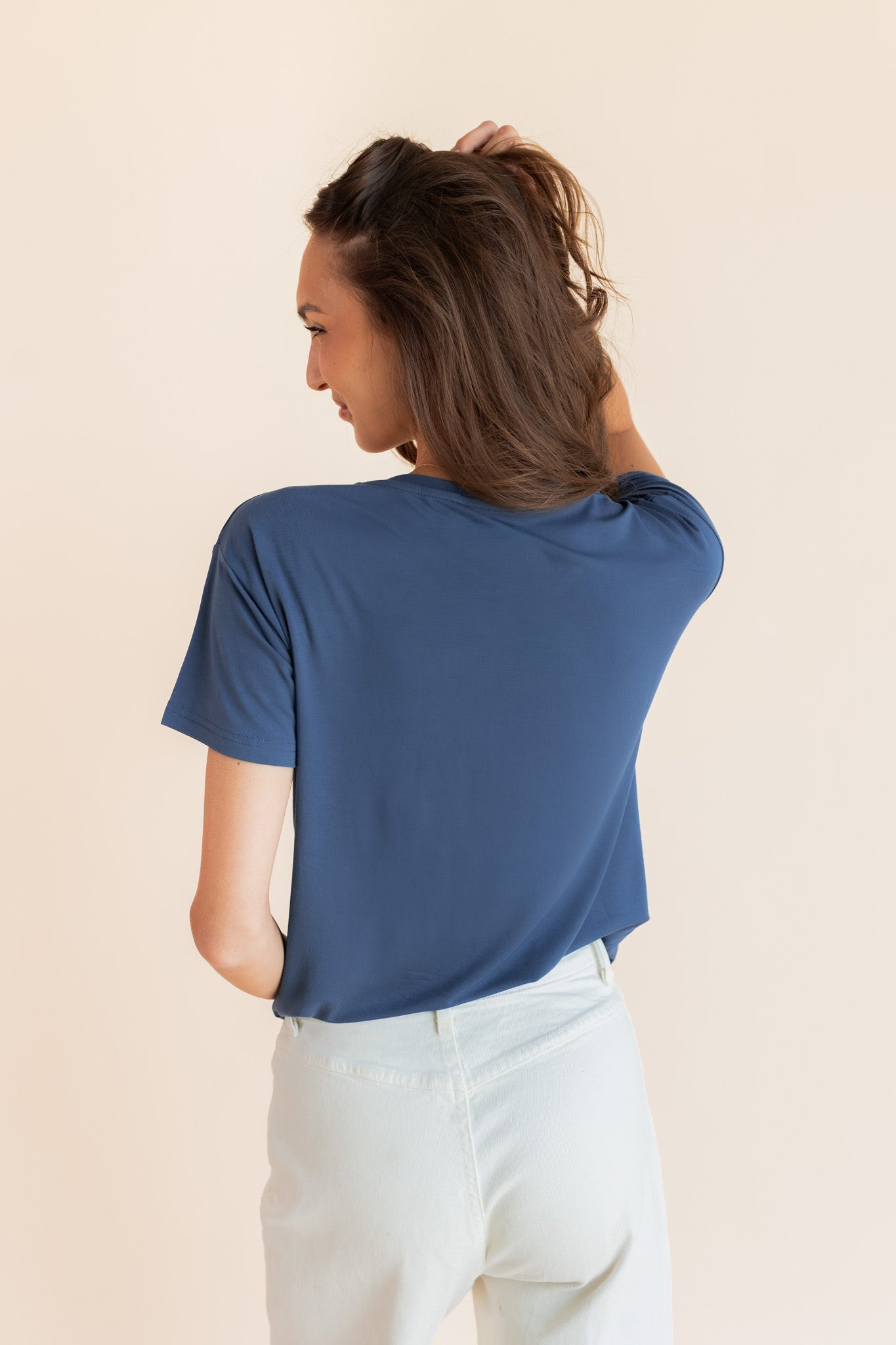 Model showcasing back side of Women's Oversized V-Neck Tee in Oxford over white pants on a beige background