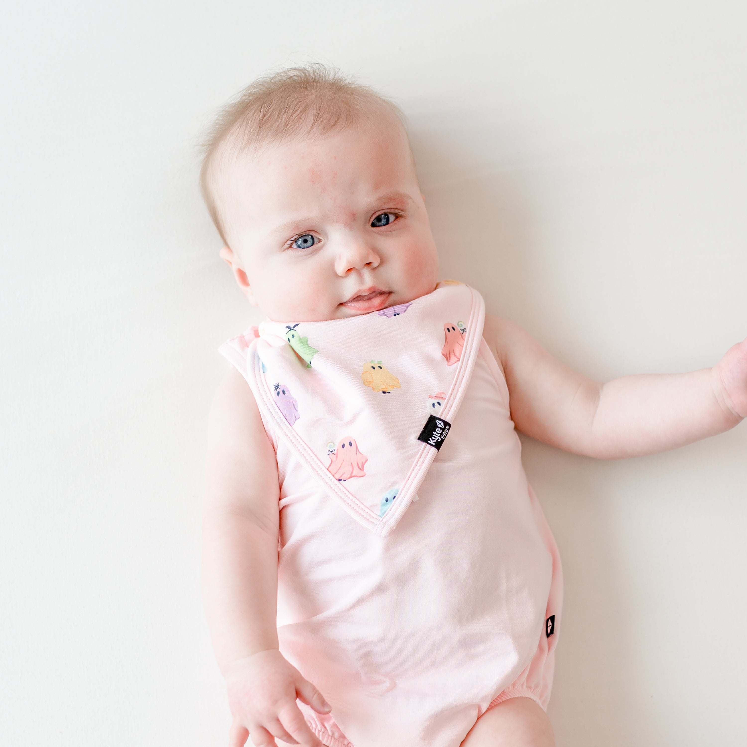 Infant laying on a light neutral background wearing the Bib in Pastel Ghost paired with a Sakura Spaghetti strap leotard