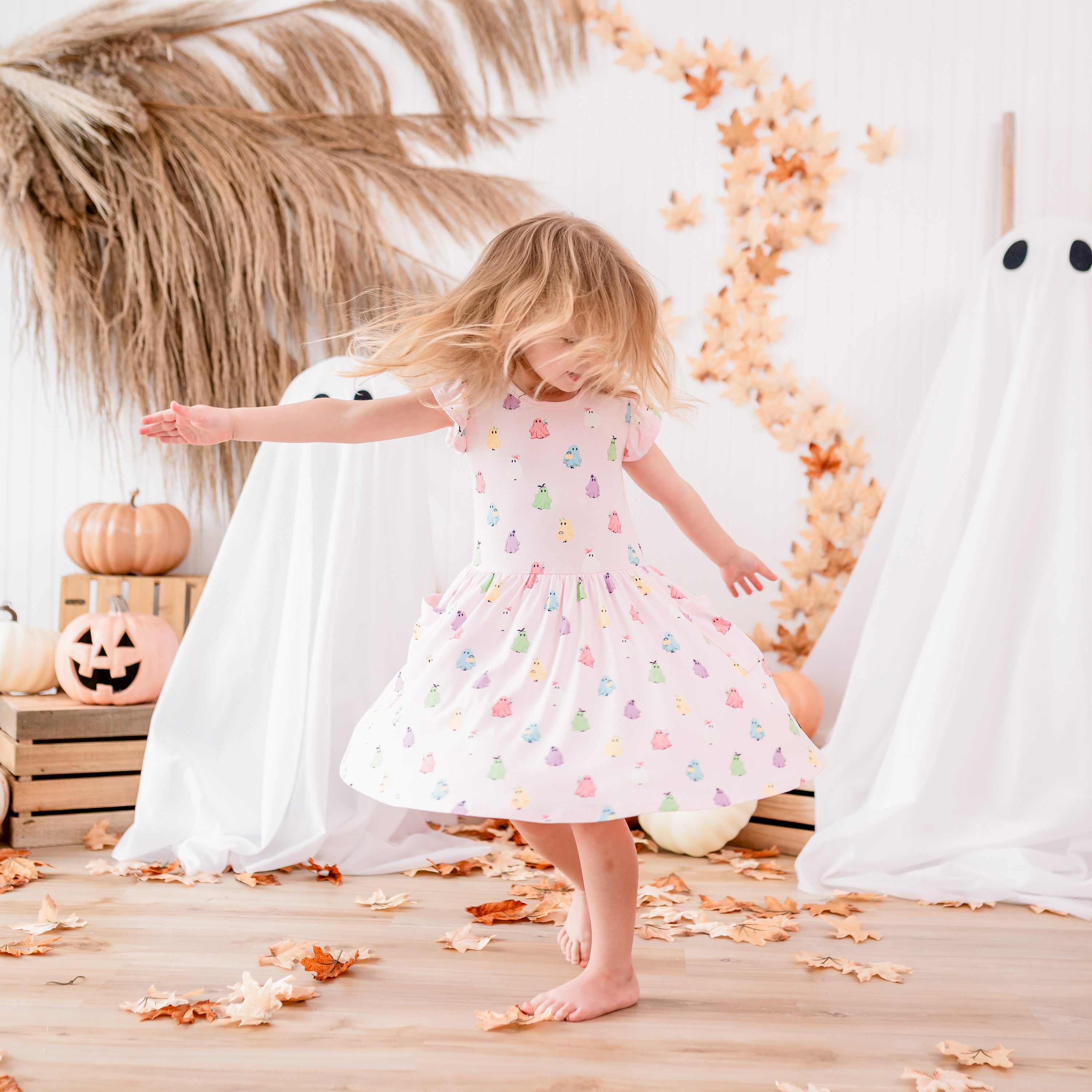 Young girl twirling in her Pocket Dress in Pastel Ghost in front of a fall backdrop