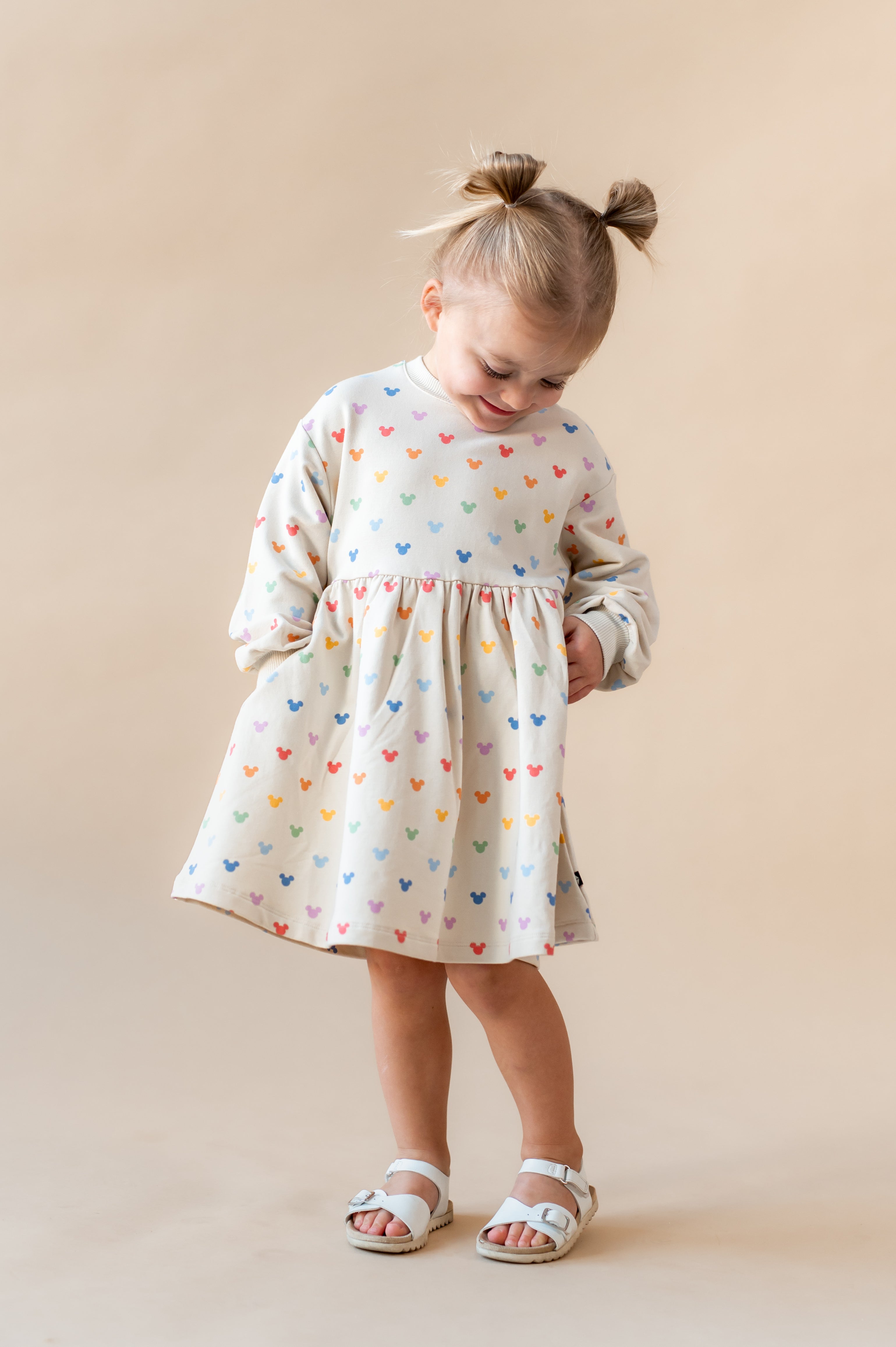 Girl looking down with her hands in her pocket wearing pastel mickey dress.