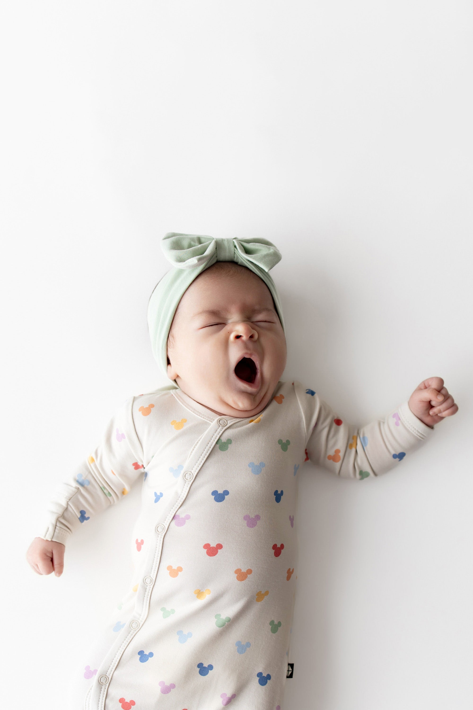 Baby yawning wearing a Mickey Mouse printed bundler and green bow