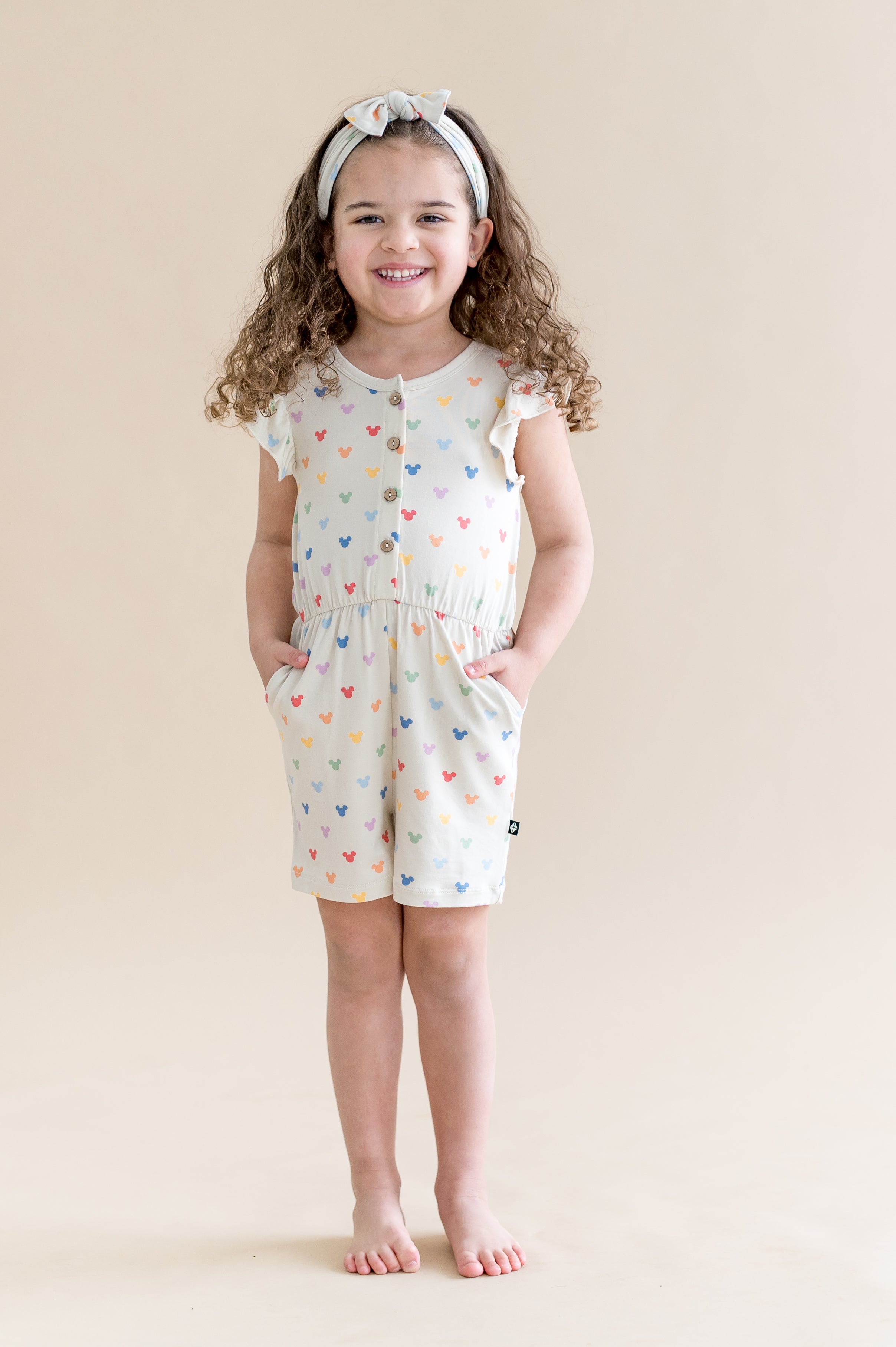 Child wearing cream flutter sleeve romper with a pastel mickey head print