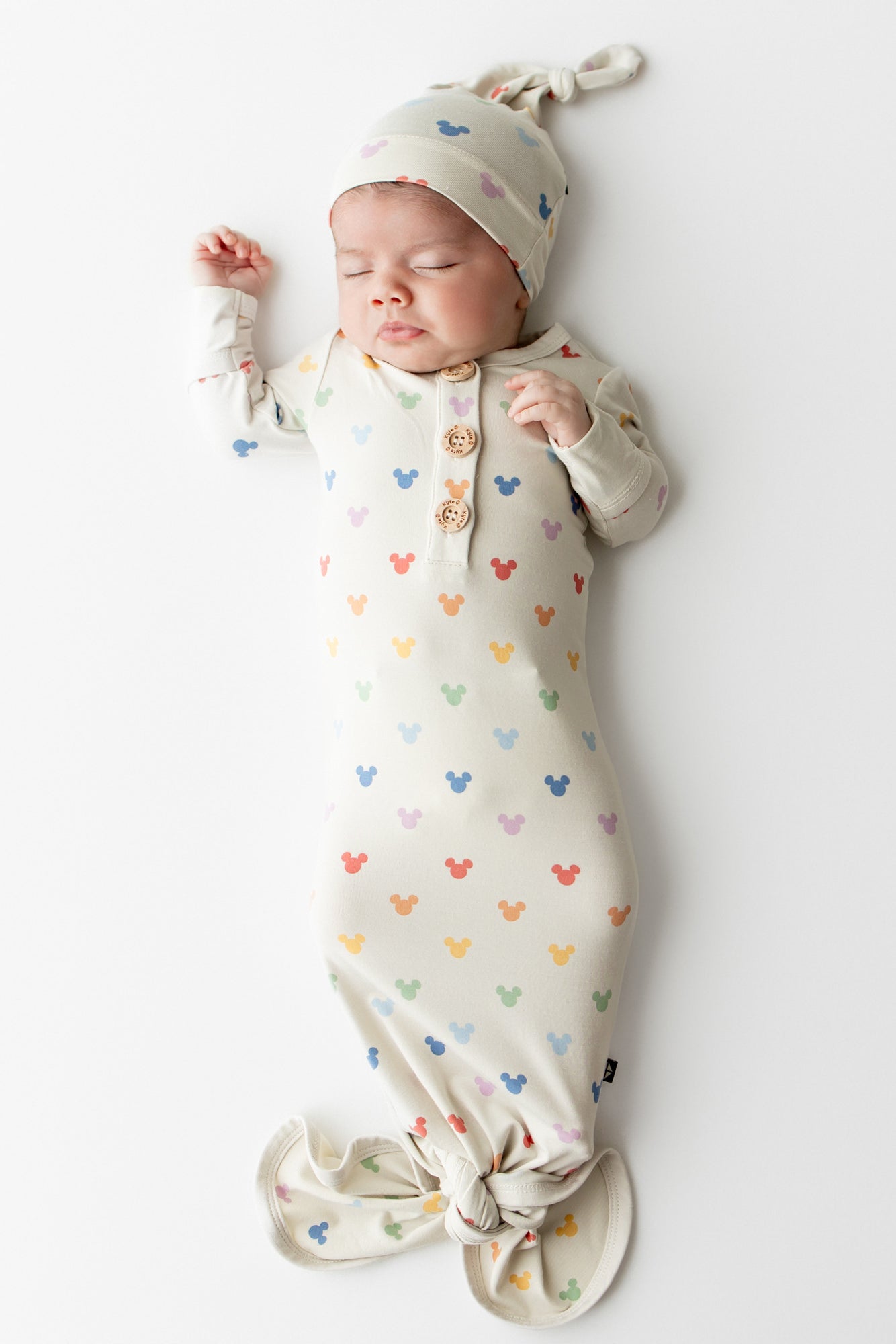 Newborn baby wrapped in a colorful mickey-patterned swaddle and wearing a matching hat on a white background