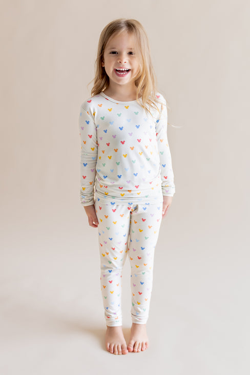 Girl smiling in Long Sleeve Pajamas in Pastel Mickey Mouse print on a cream background