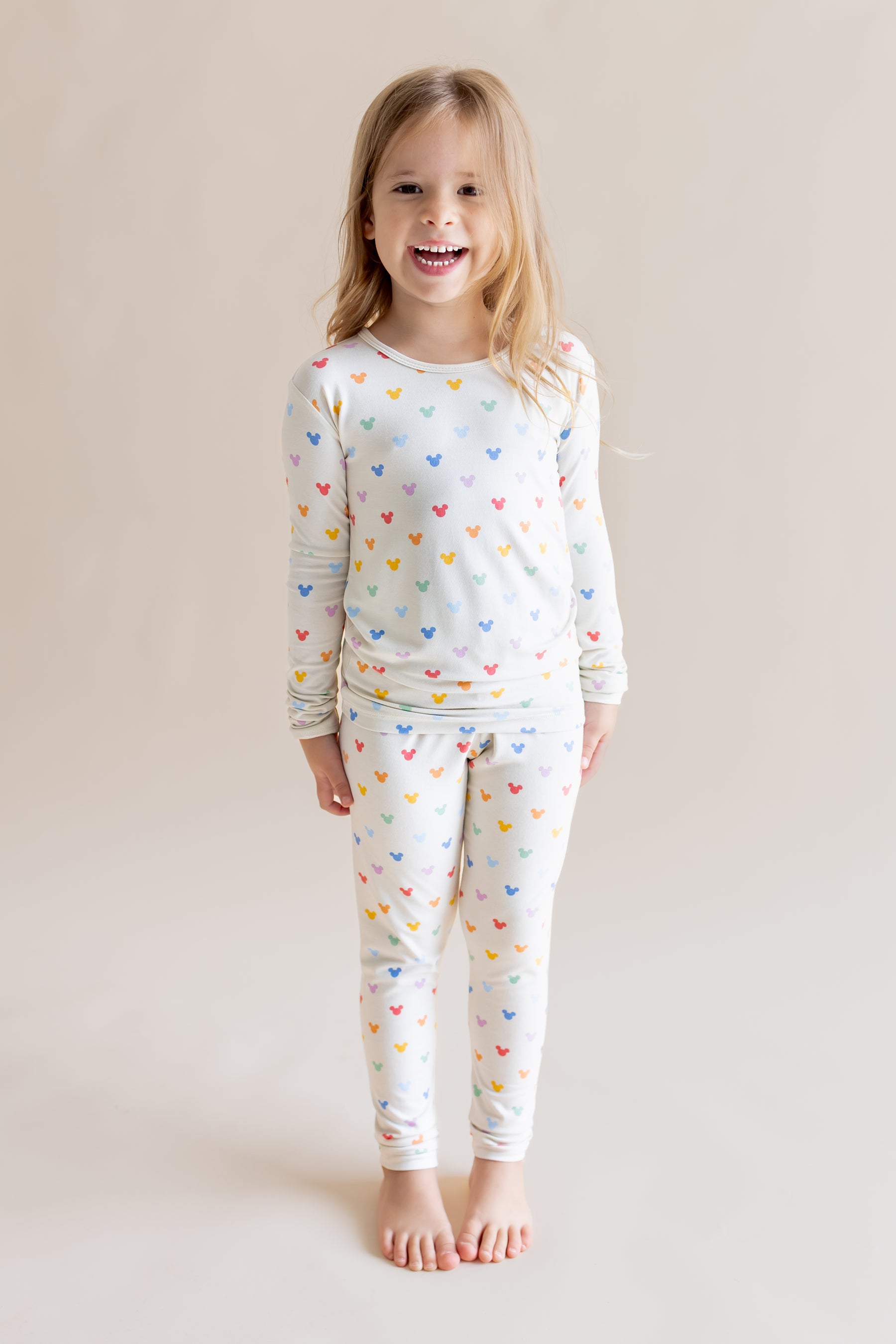 Girl smiling in Long Sleeve Pajamas in Pastel Mickey Mouse print on a cream background