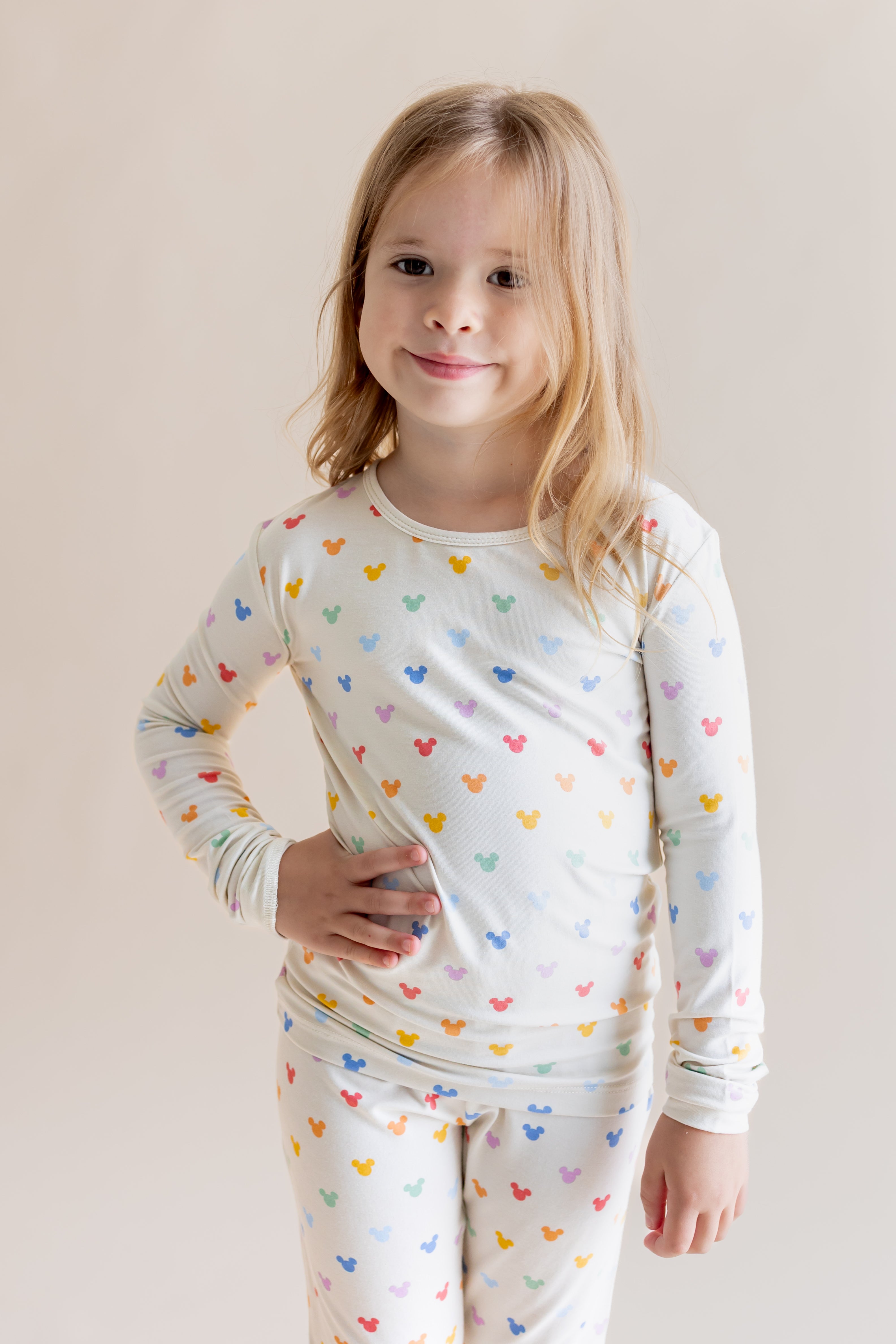 Girl posing in Long Sleeve Pajamas in Pastel Mickey Mouse print on a cream background