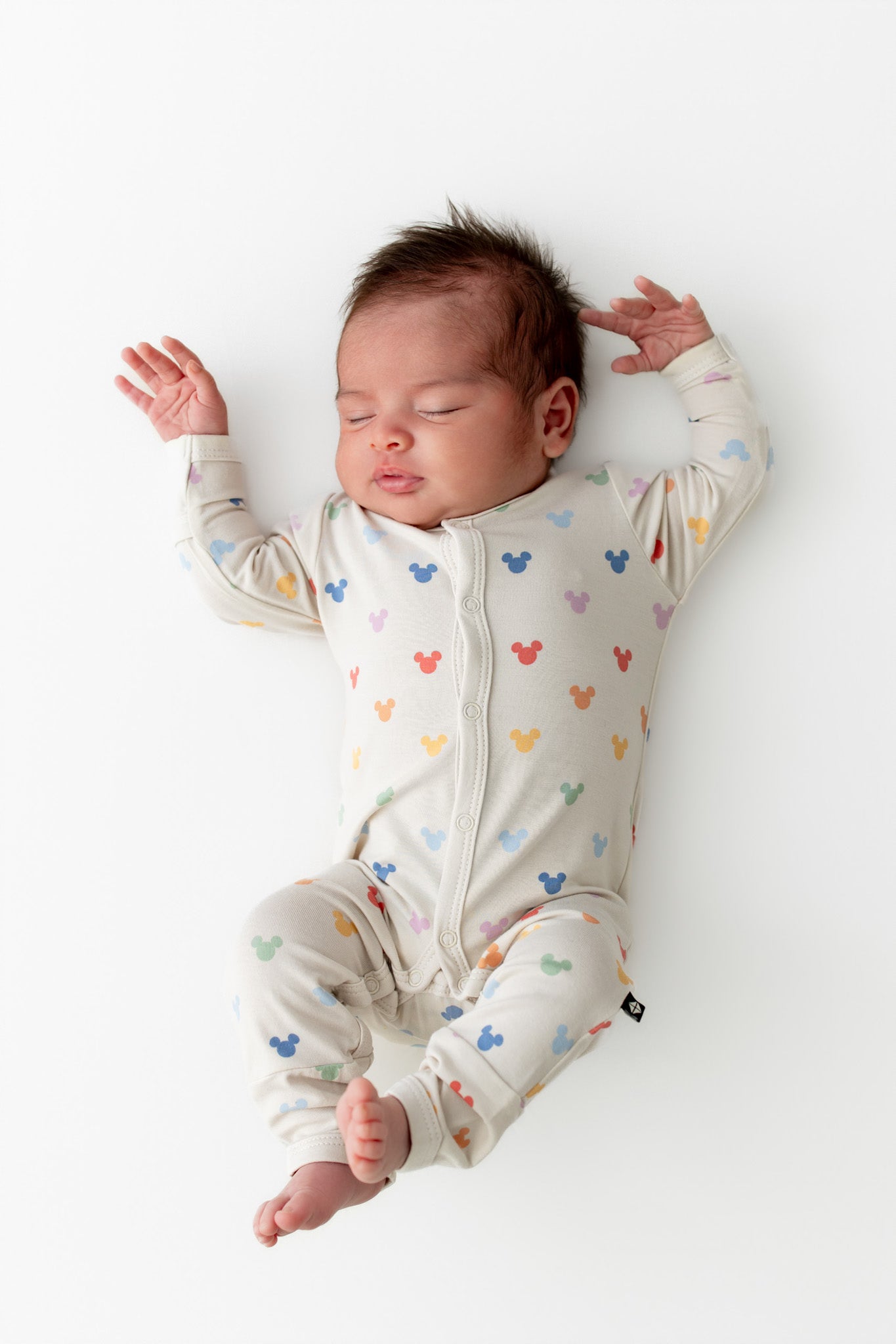 Baby asleep wearing snap romper with pastel mickey pattern
