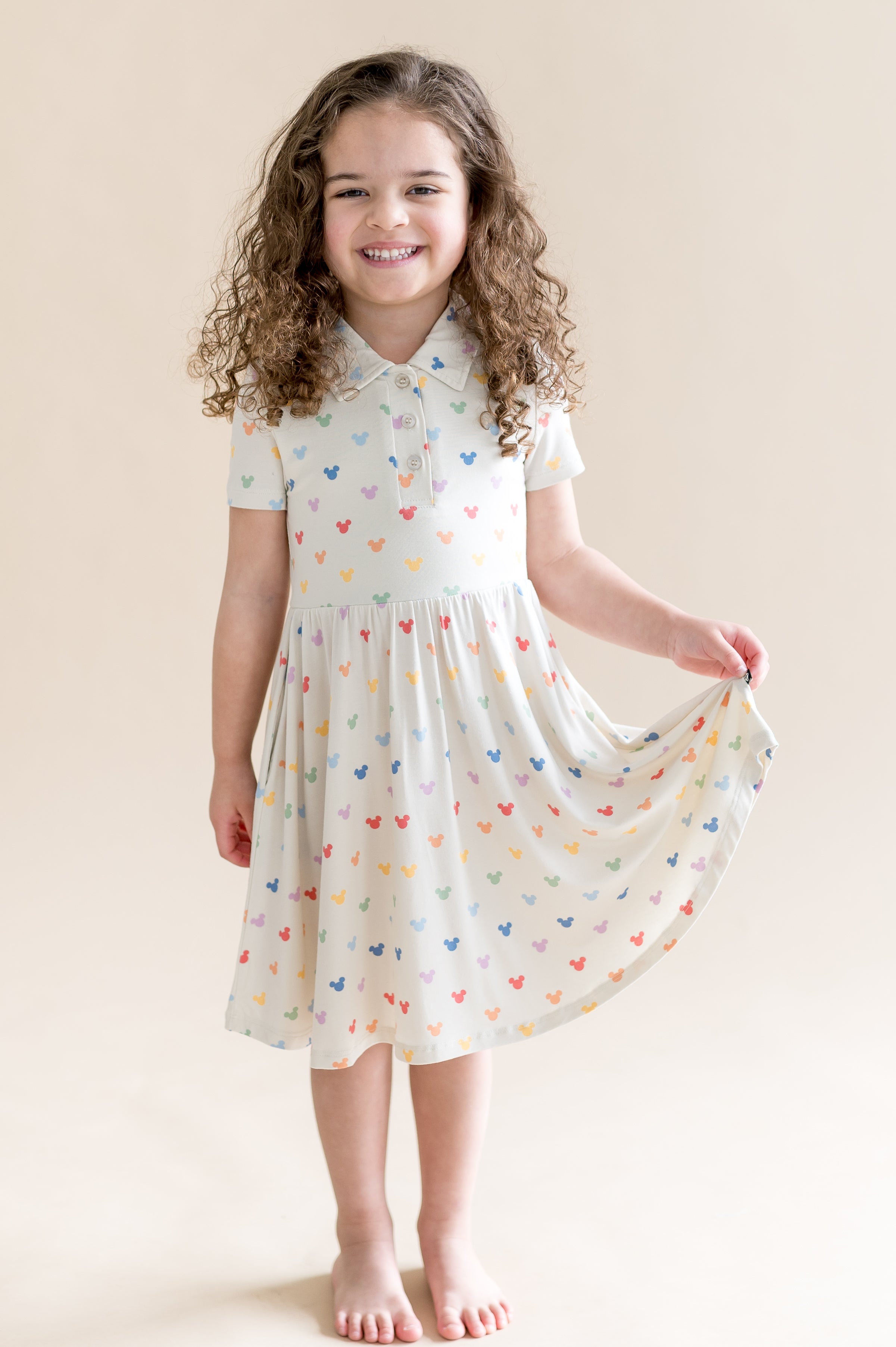 Young girl wearing a cream dress with colorful mickey patterns against a beige background