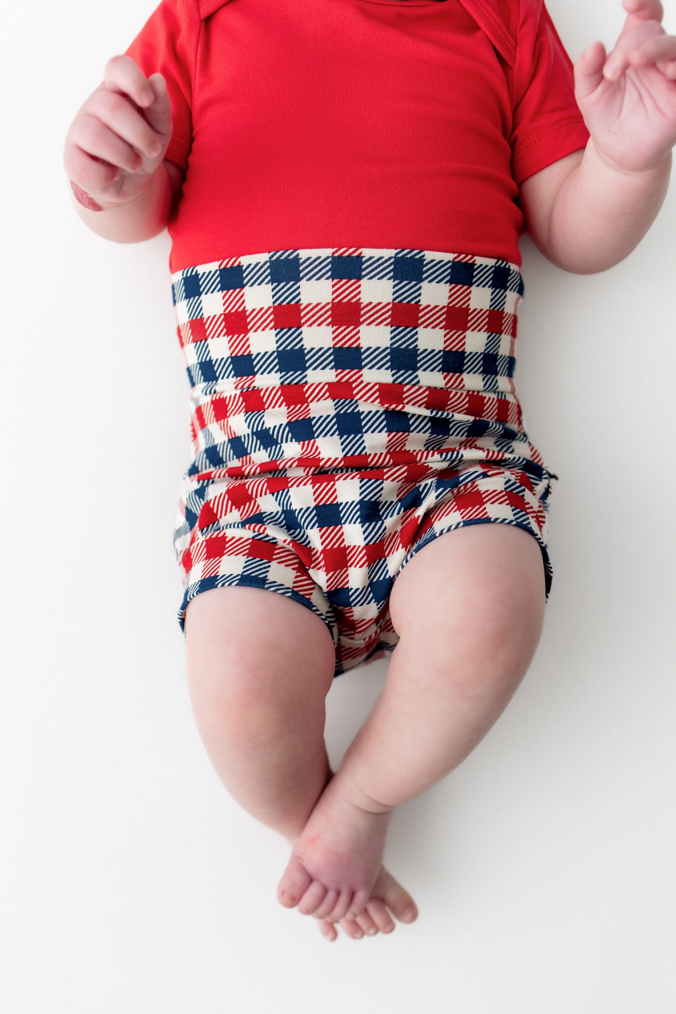 Baby wearing a red blue and white Patriotic Gingham check print bummies over a red bodysuit on a white background
