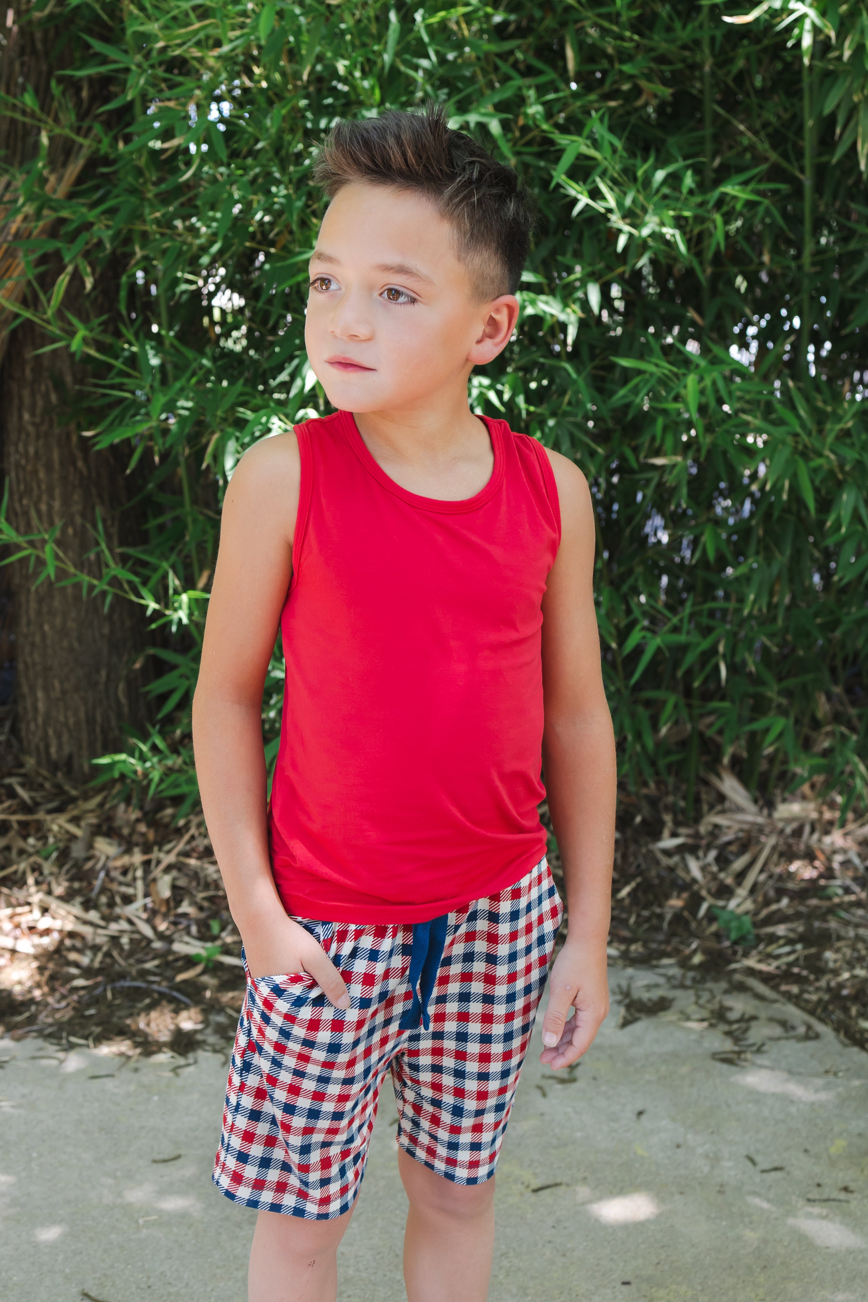 Child wearing a red blue and white Patriotic Gingham check print drawstring shorts over a red  tank top outdoors