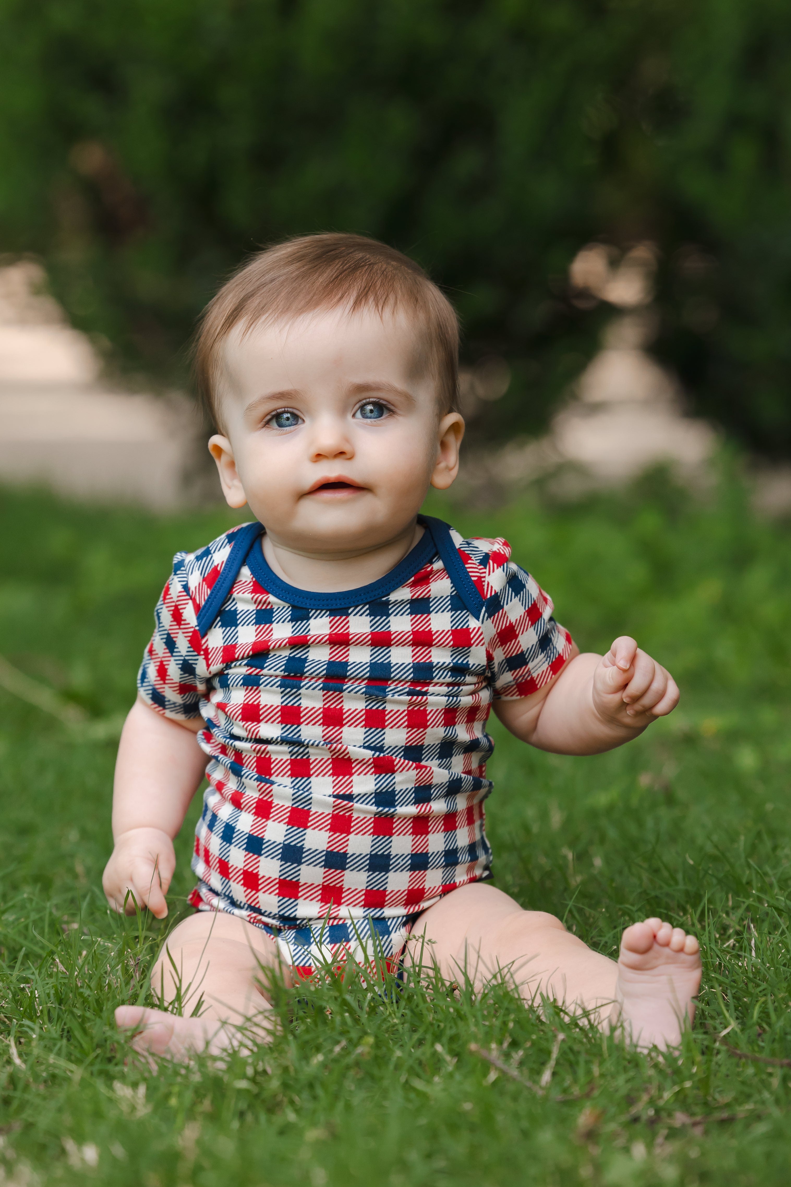 Baby wearing a red blue and white Patriotic Gingham check print short sleeve Bodysuit sitting on a grass