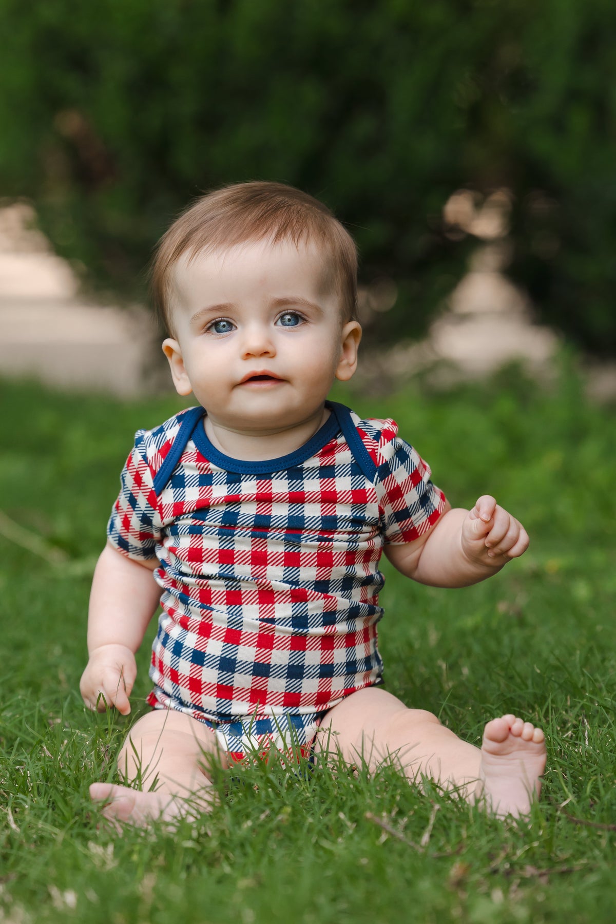 Baby wearing a red blue and white Patriotic Gingham check print short sleeve Bodysuit sitting on a grass