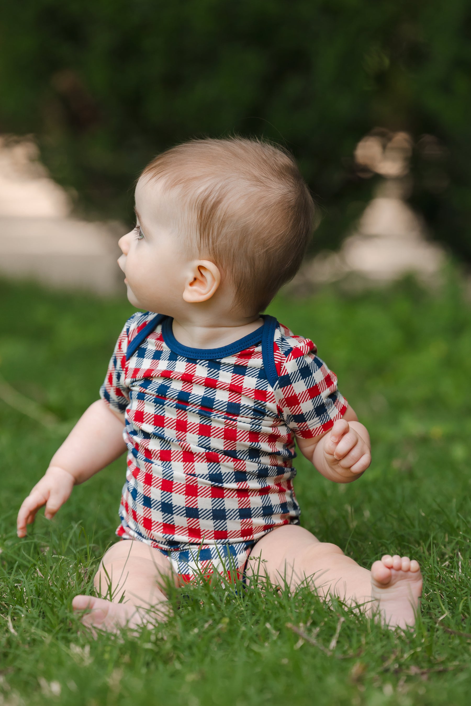 Baby wearing a red blue and white Patriotic Gingham check print short sleeve Bodysuit sitting on a grass