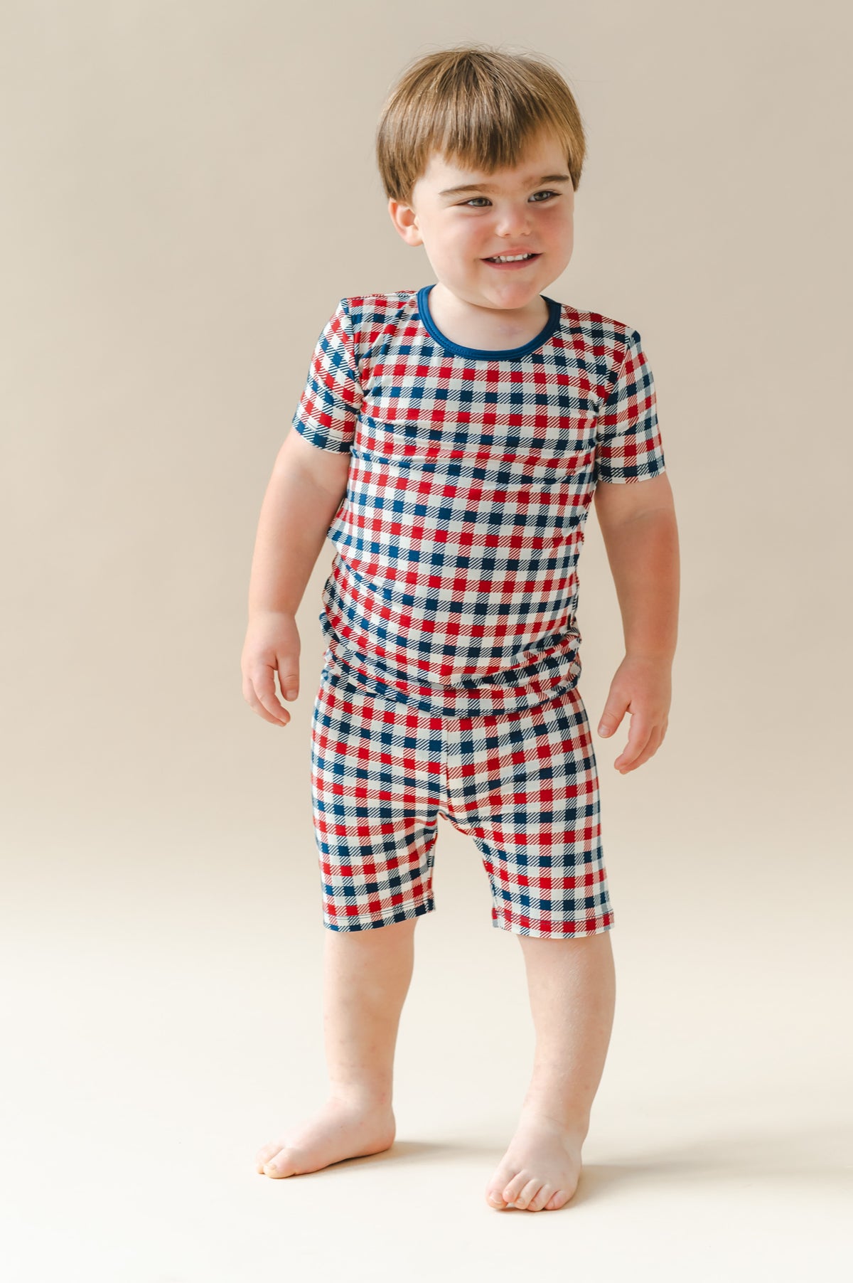 Child wearing Short Sleeve Pajamas in red blue and white Patriotic Gingham check print on a beige background