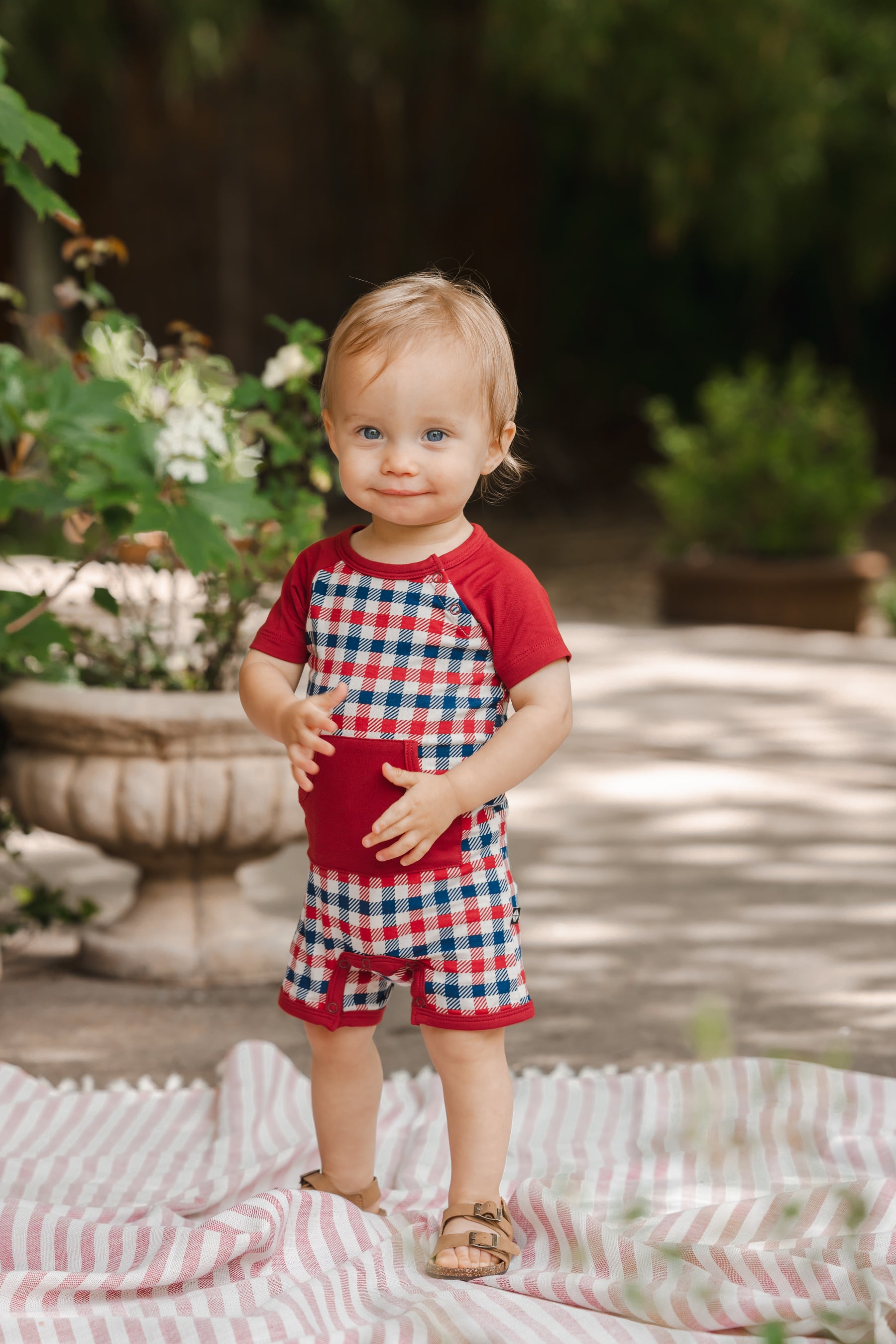 Child standing outdoors wearing a red blue and white Patriotic Gingham check print shortall 
