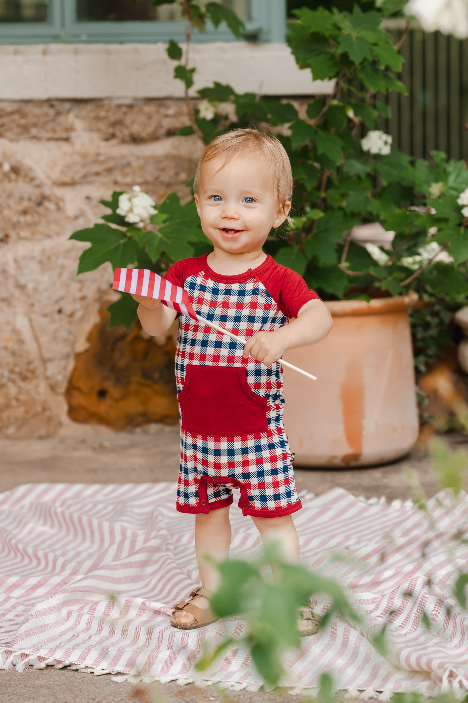 Child playing outdoors in red blue and white Patriotic Gingham check print shortall with a flag