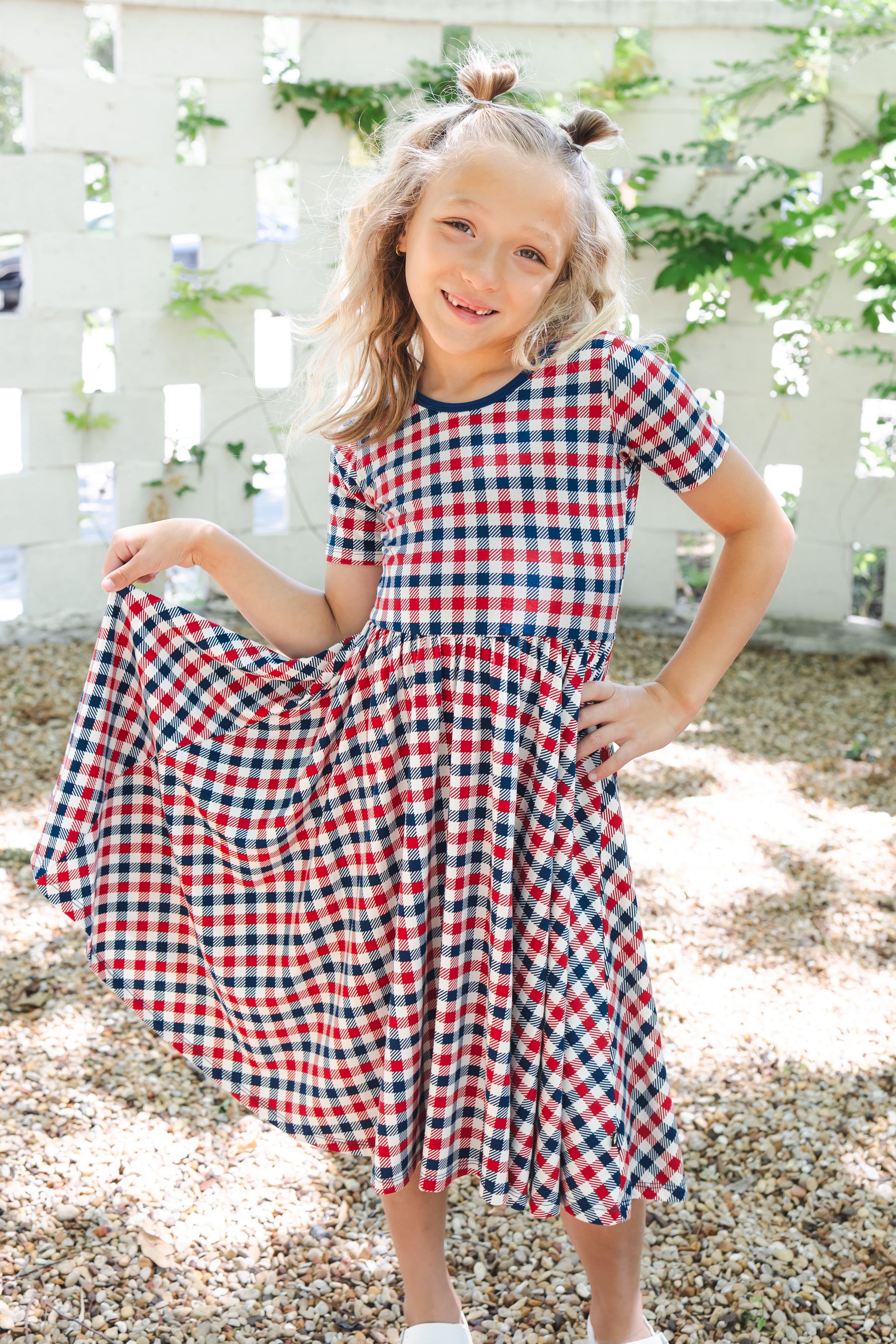 Child standing outdoors wearing a Twirl Dress in Red blue and white Patriotic Gingham check print 