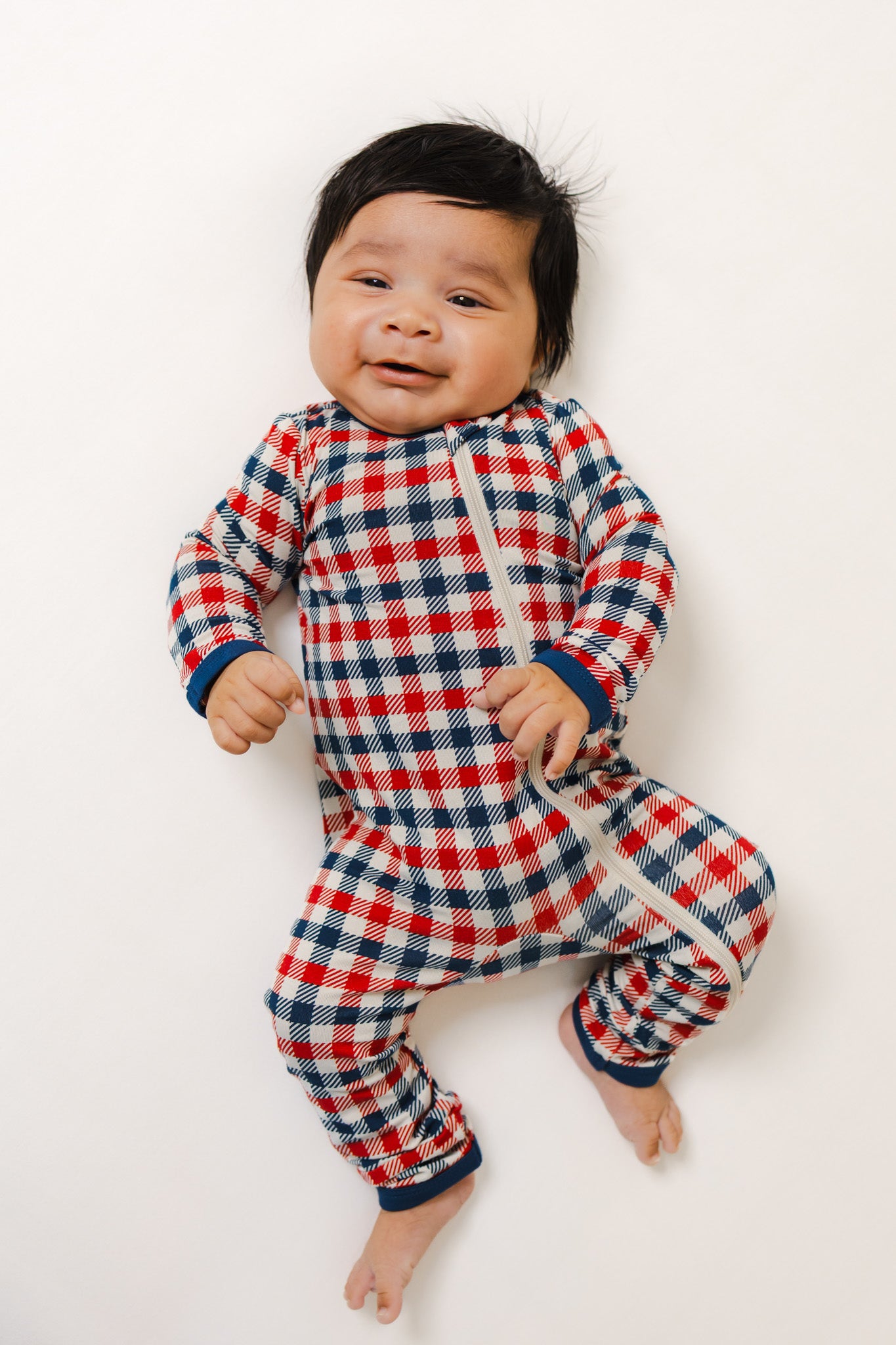 Baby wearing zippered romper in red blue and white Patriotic Gingham check print on a white background