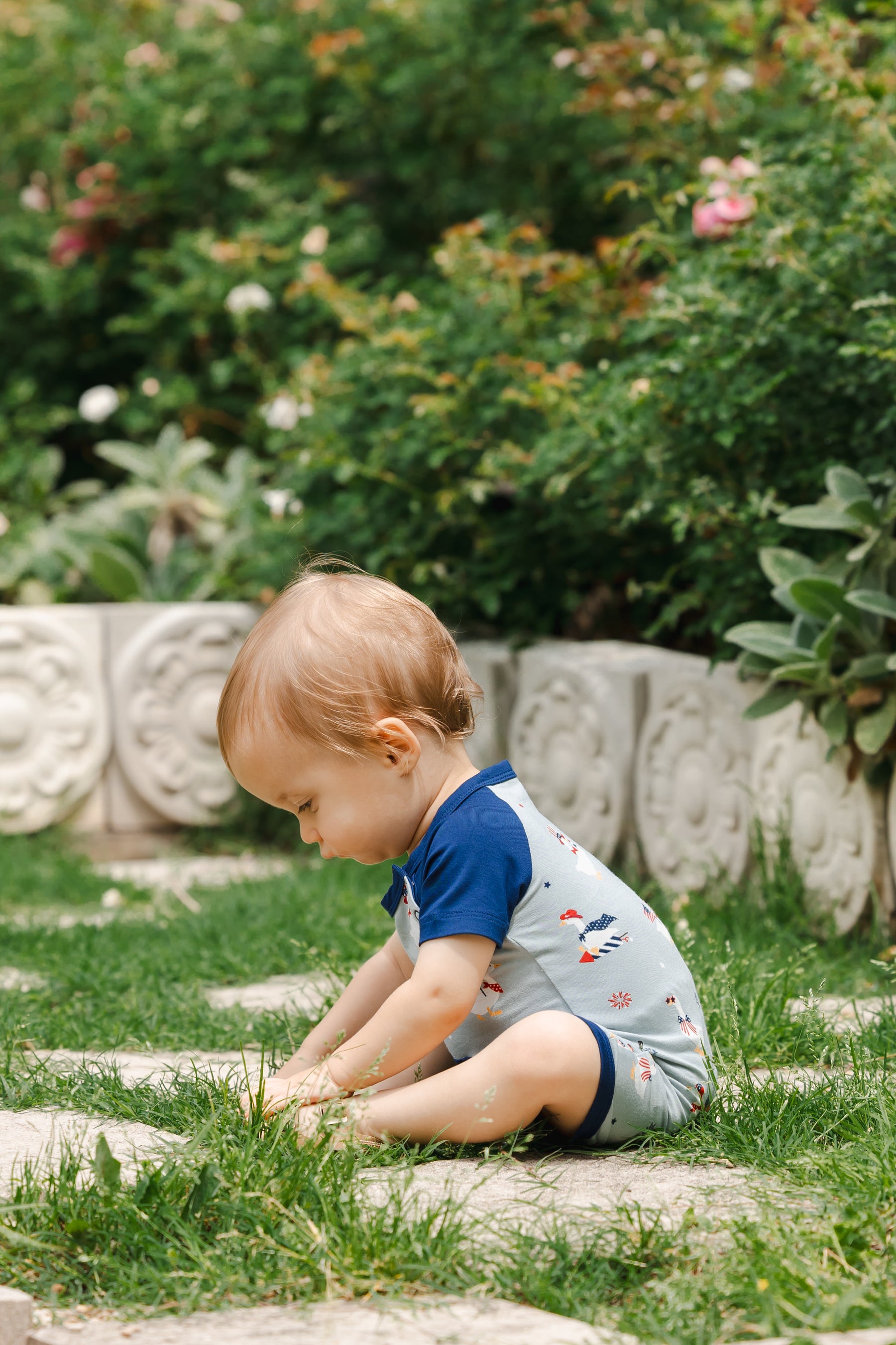 Child sitting in light blue Shortall in Patriotic Goose print with navy trim outdoors