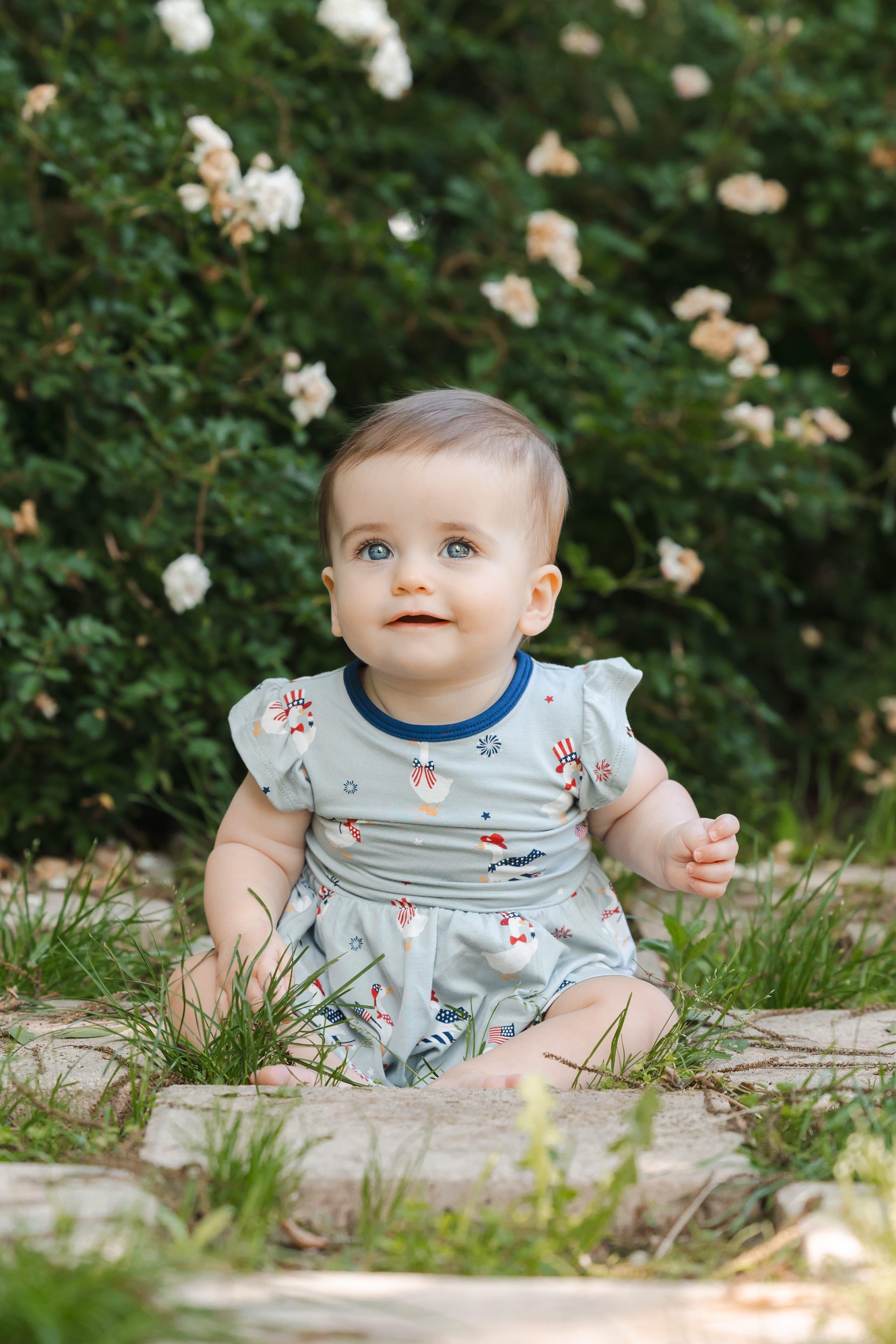 Baby sitting in a Light blue Twirl bodysuit dress in Patriotic Goose print outdoors