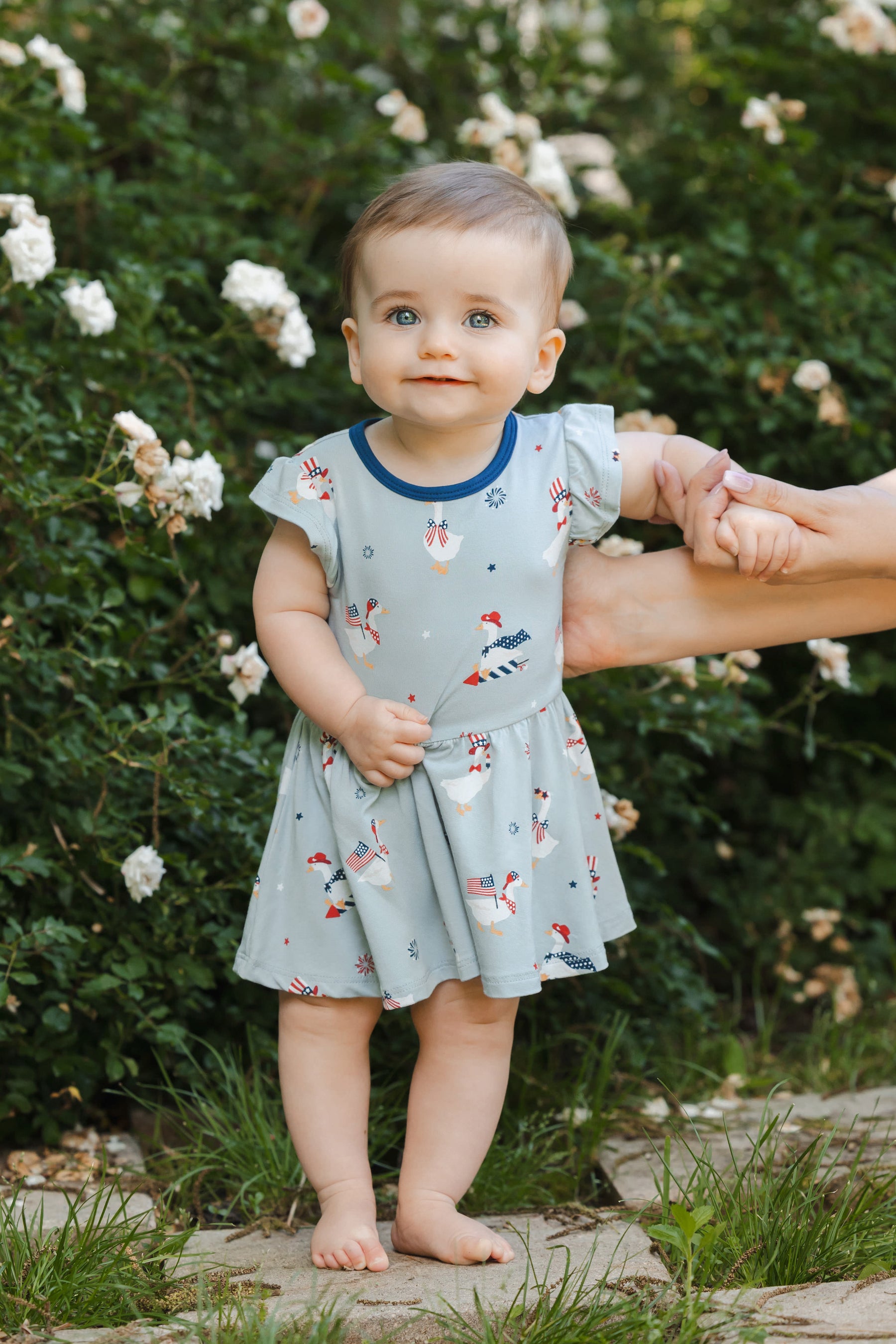 Baby wearing Light blue Twirl bodysuit dress in Patriotic Goose print outdoors