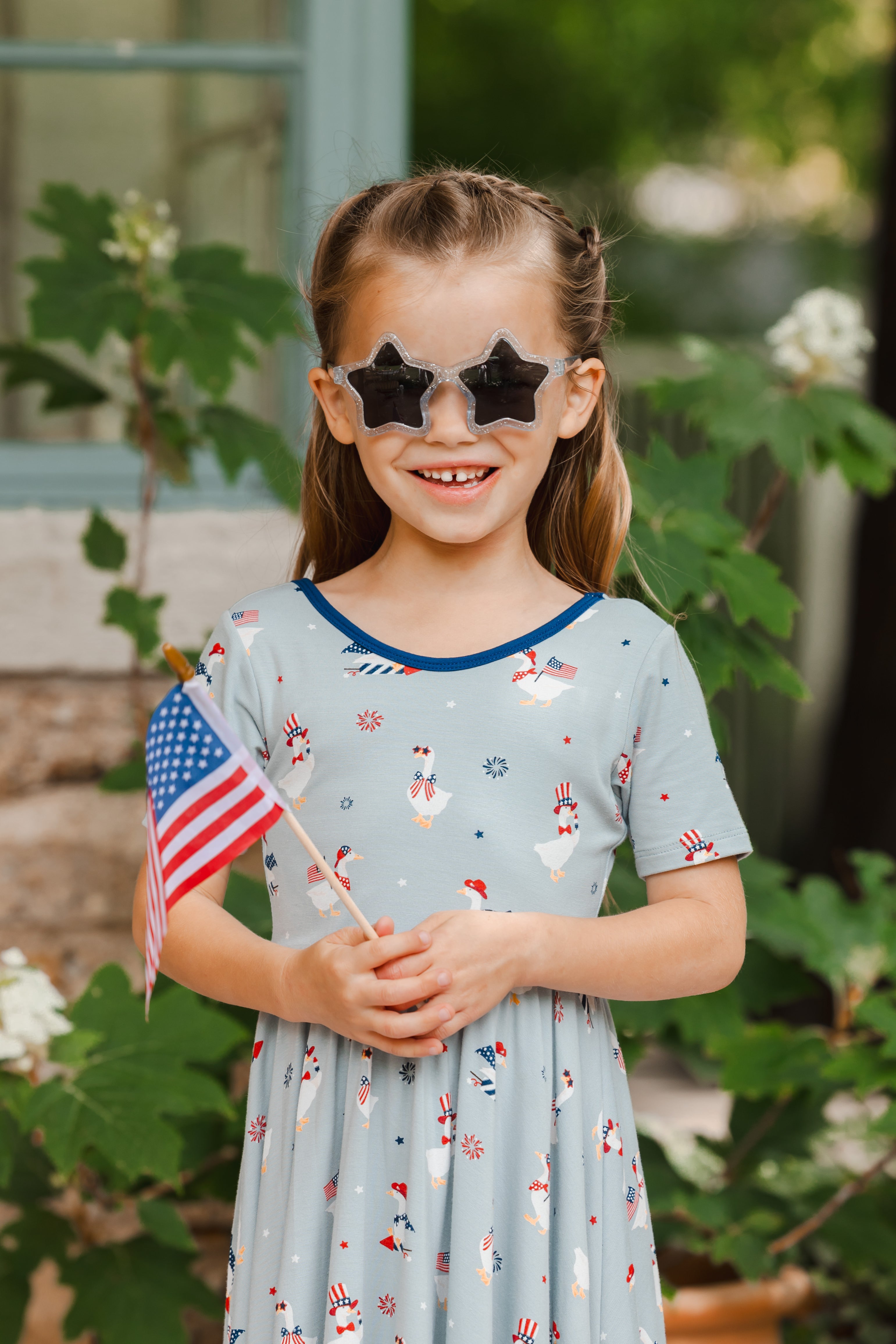 Child wearing Patriotic Goose print light blue Twirl dress and sunglasses holding a flag outdoors