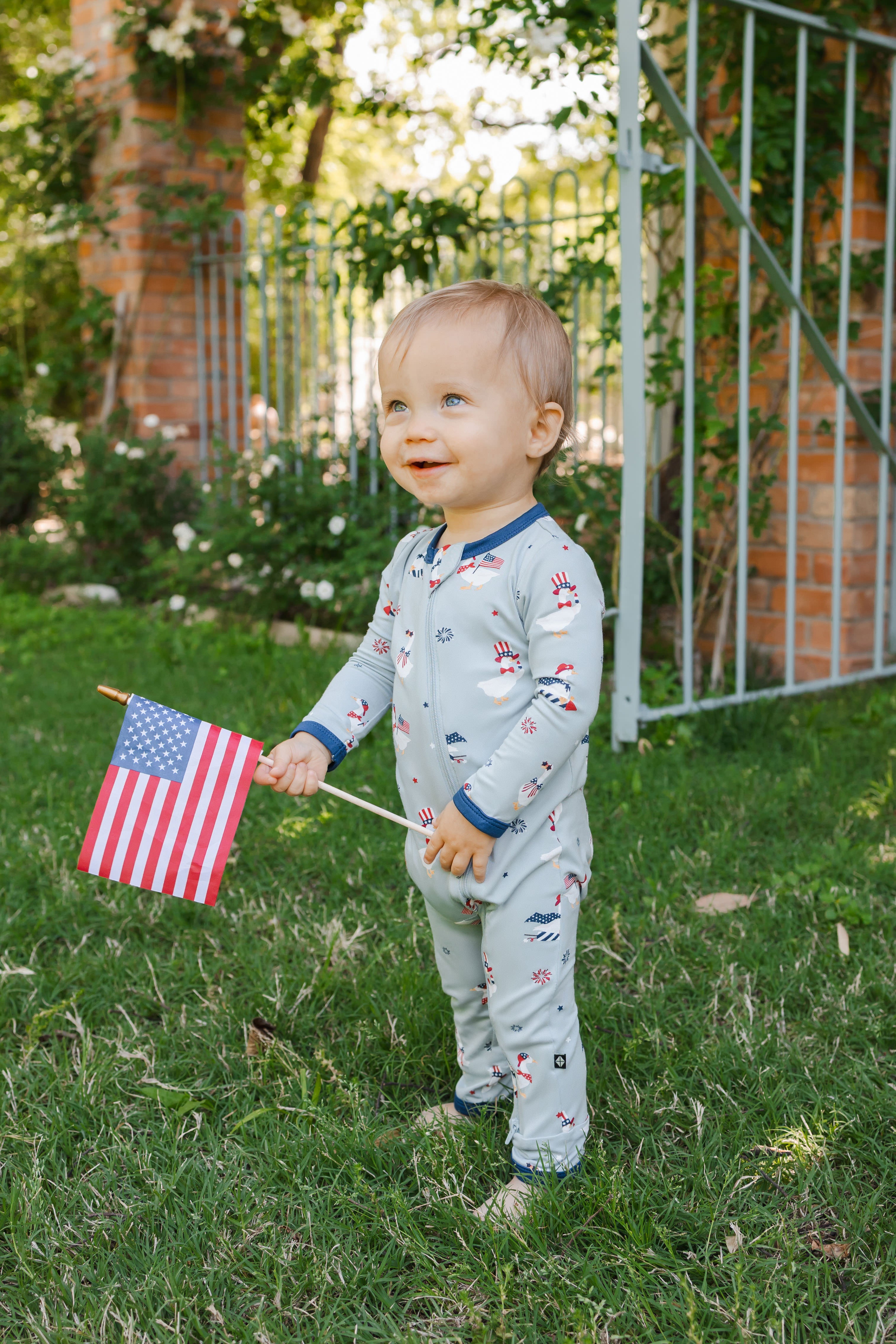 Child wearing Patriotic Goose print Light blue zippered romper with a flag outdoors