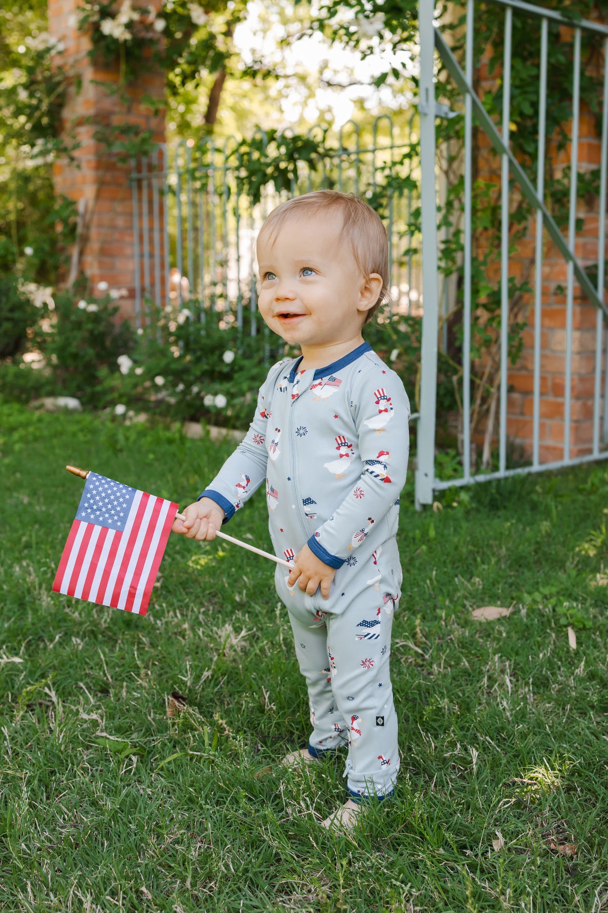 Child wearing Patriotic Goose print Light blue zippered romper with a flag outdoors