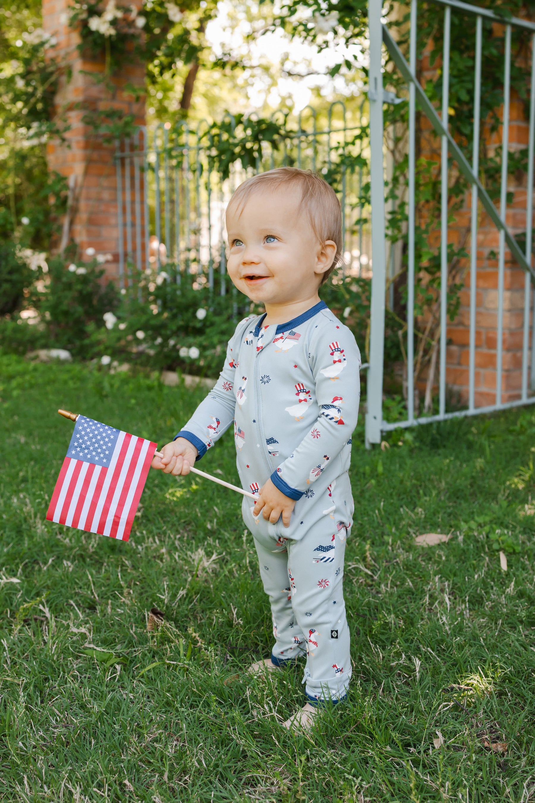 Child wearing Patriotic Goose print Light blue zippered romper with a flag outdoors