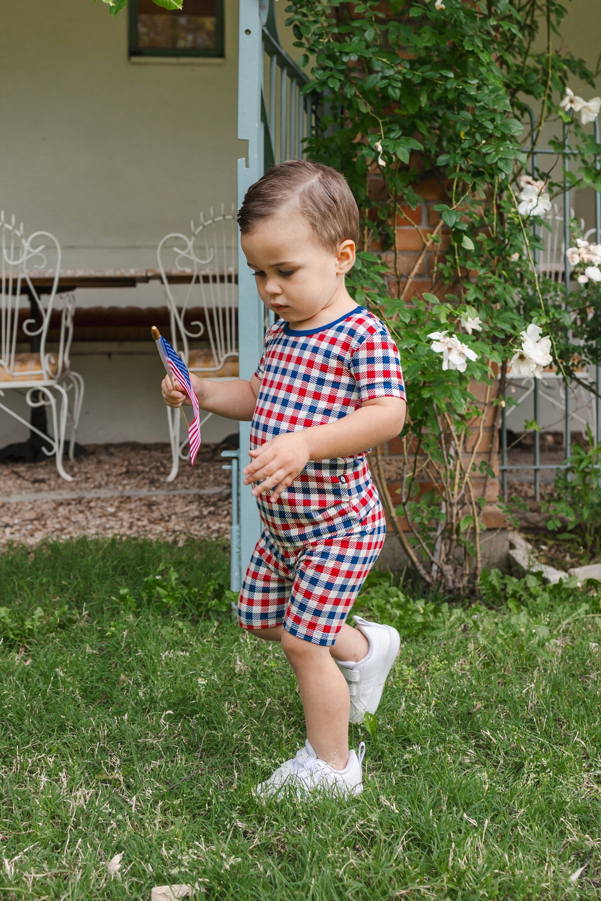 Child wearing Short Sleeve Pajamas in red blue and white Patriotic Gingham check print on a grass with a flag