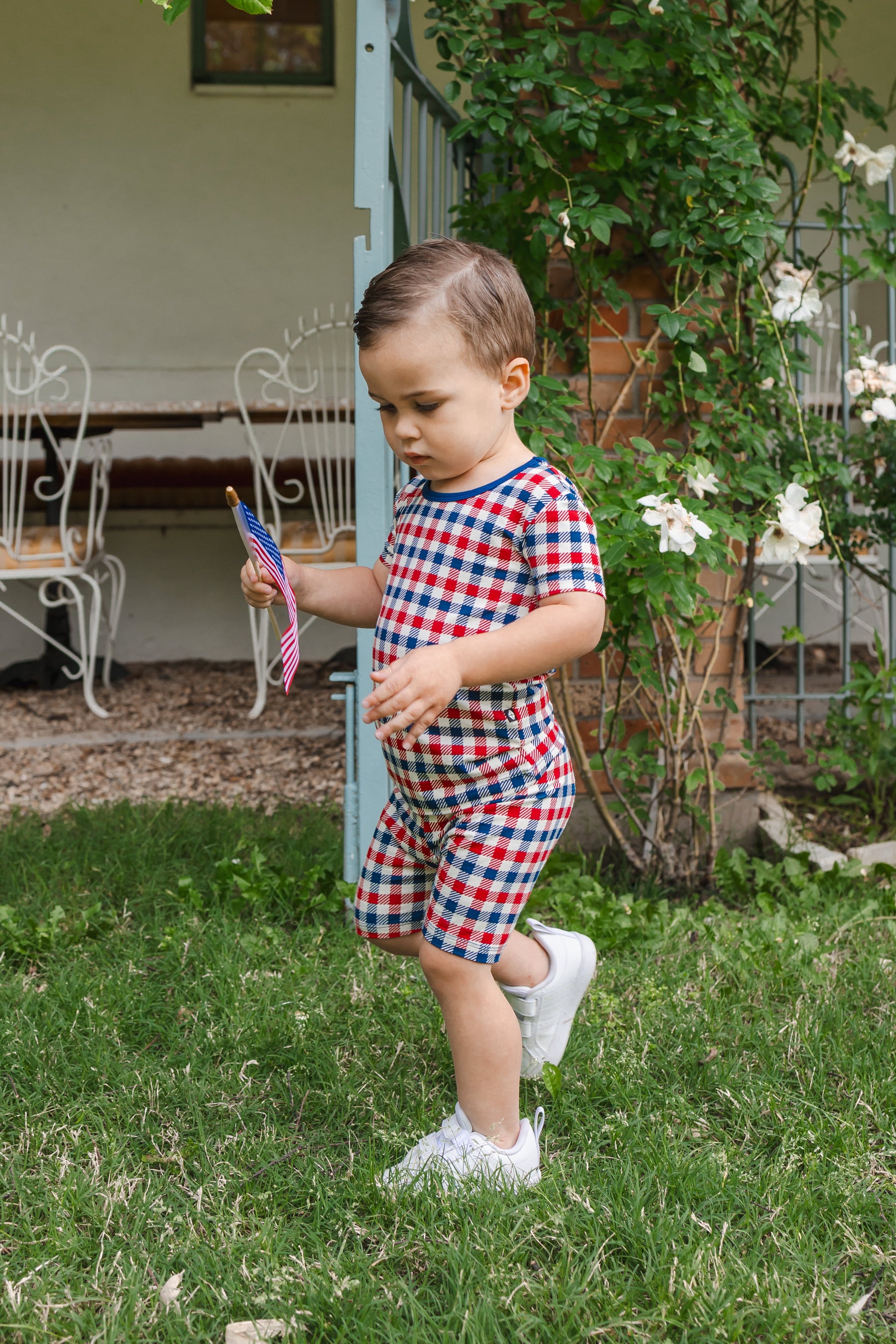 Child wearing Short Sleeve Pajamas in red blue and white Patriotic Gingham check print on a grass with a flag