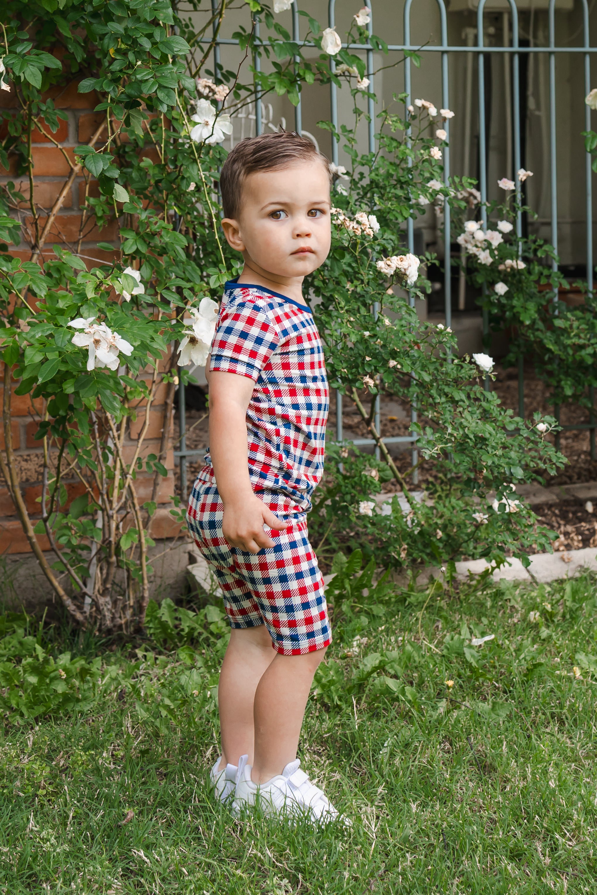 Child wearing Short Sleeve Pajamas in red blue and white Patriotic Gingham check print on a grass