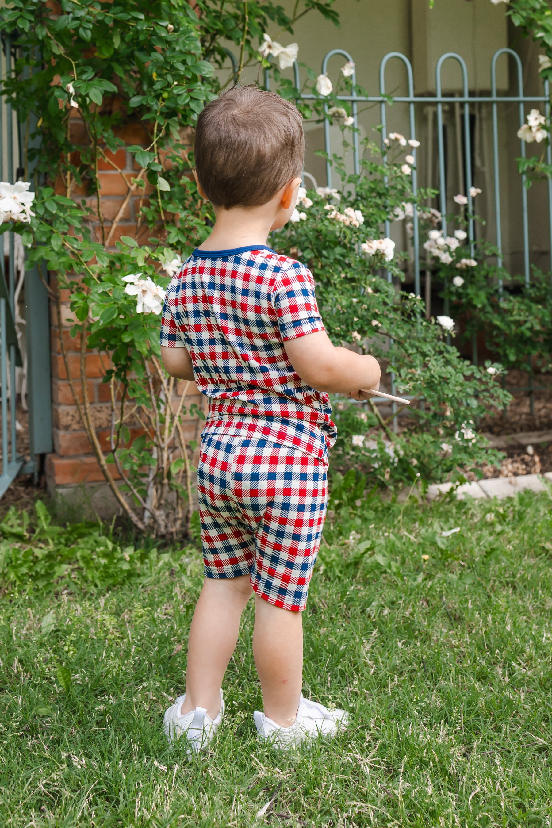 Back side of a child wearing Short Sleeve Pajamas in red blue and white Patriotic Gingham check print outdoors on a grass