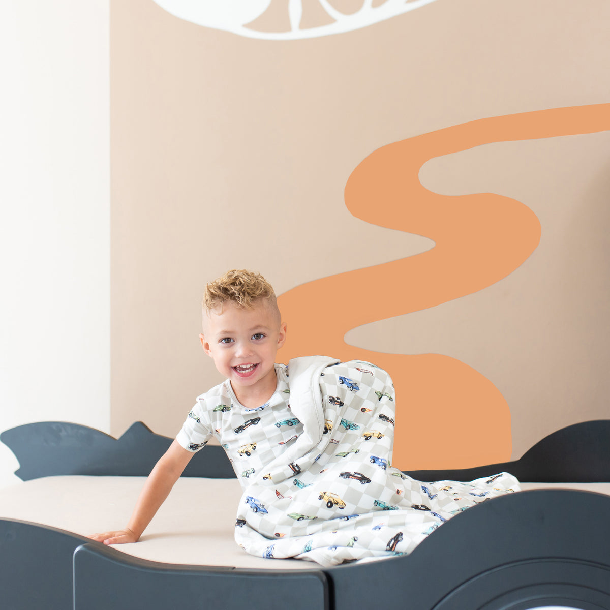 Young child sitting with one arm propped on a bed with the Toddler Blanket in Fast and Fierce 1.0 overtop him