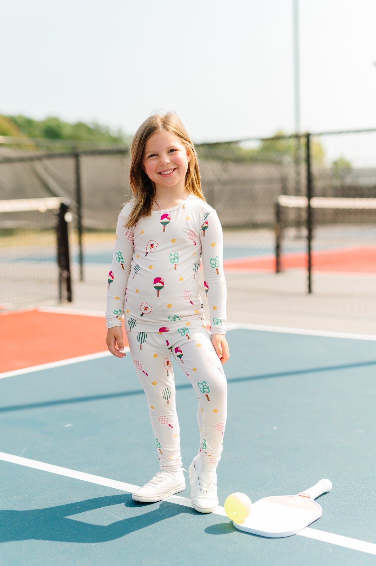 Girl wearing Long Sleeve Pajamas in Pickleball print standing on pickleball court