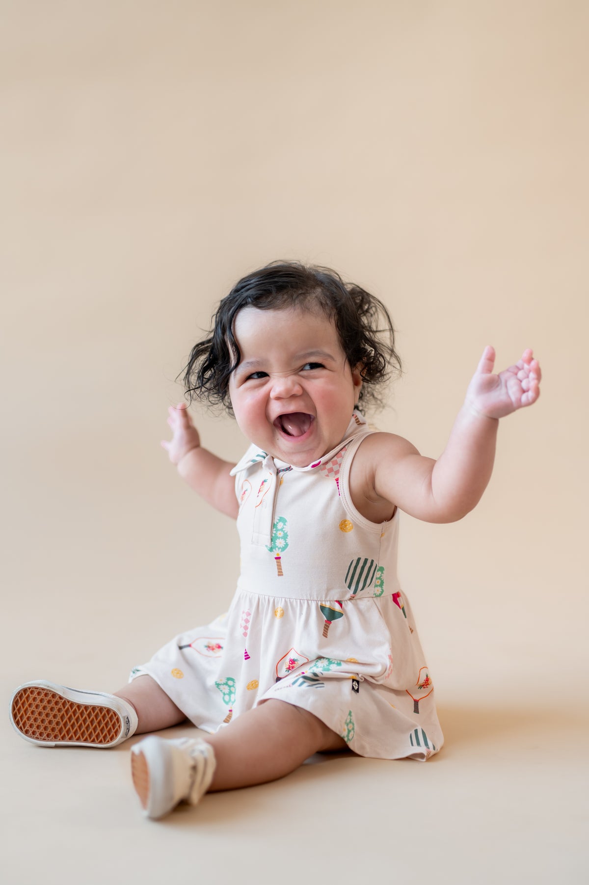 Baby laughing on beige background wearing Polo Bodysuit Dress in Pickleball print 