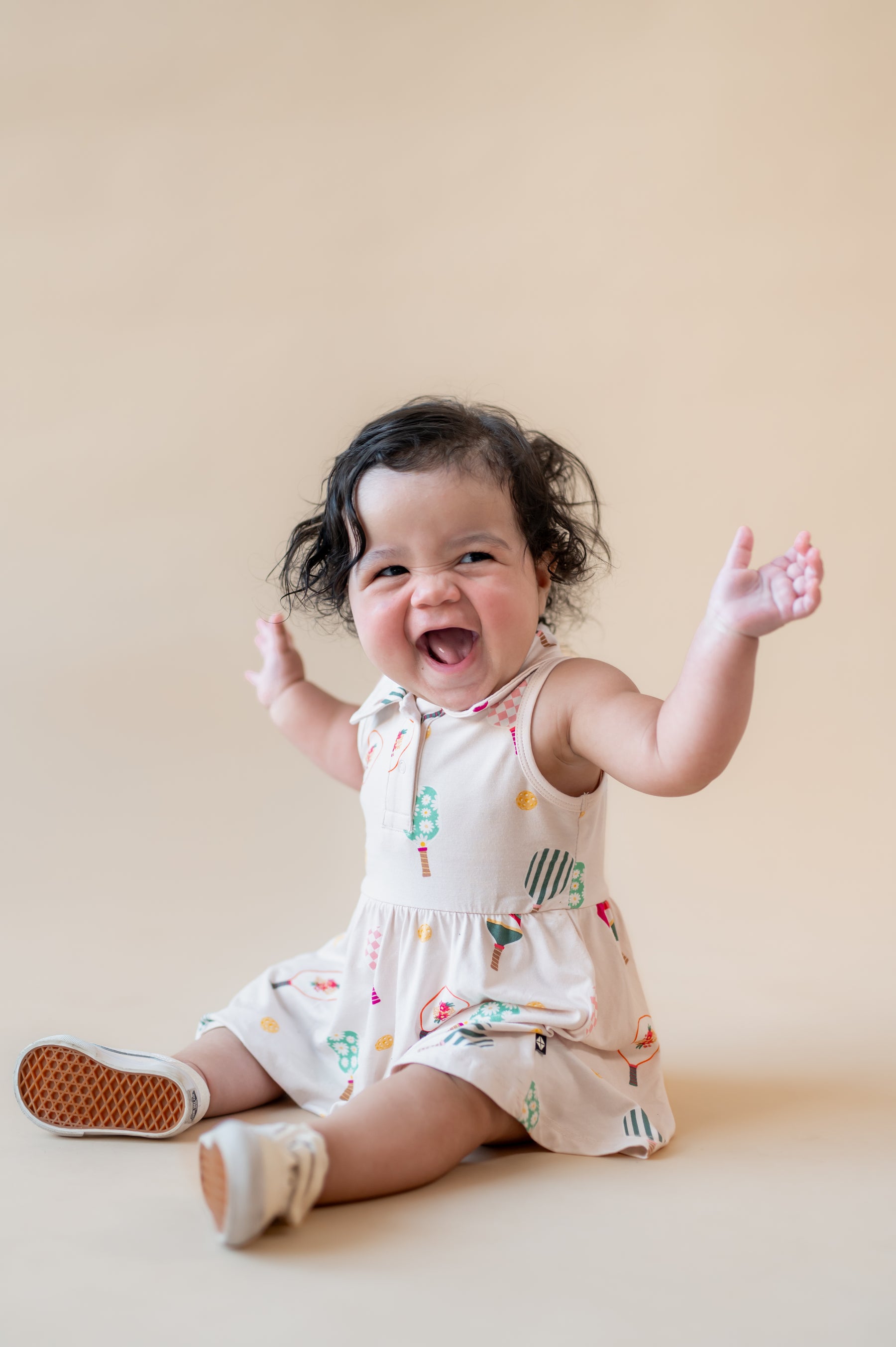 Baby laughing on beige background wearing Polo Bodysuit Dress in Pickleball print 