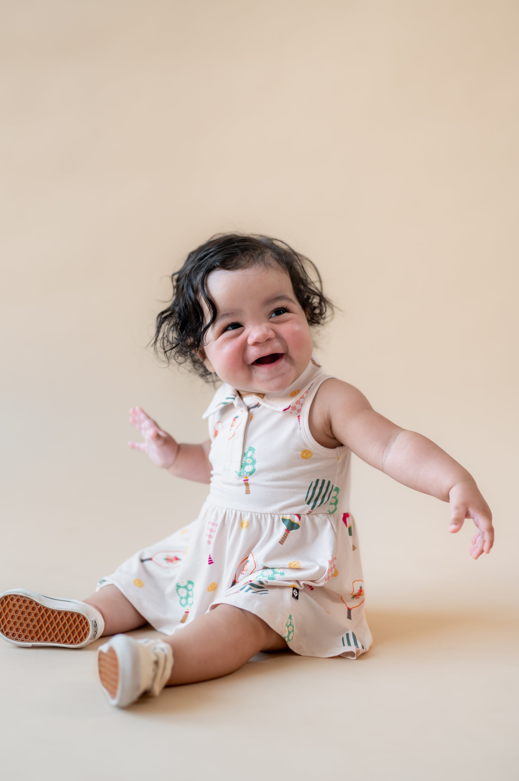 Baby posing in Polo Bodysuit Dress with Pickleball print on a beige background