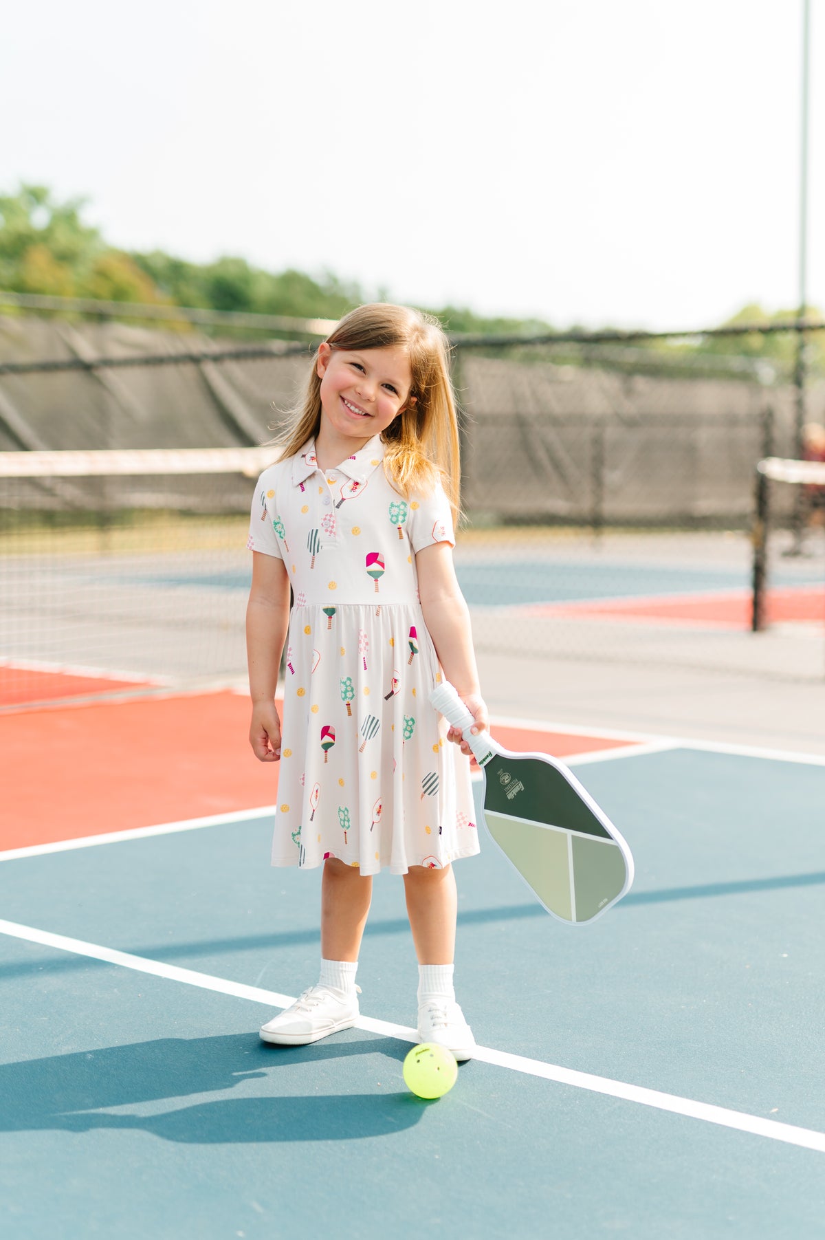 Girl smiling on pickleball court wearing Polo Dress in Pickleball print