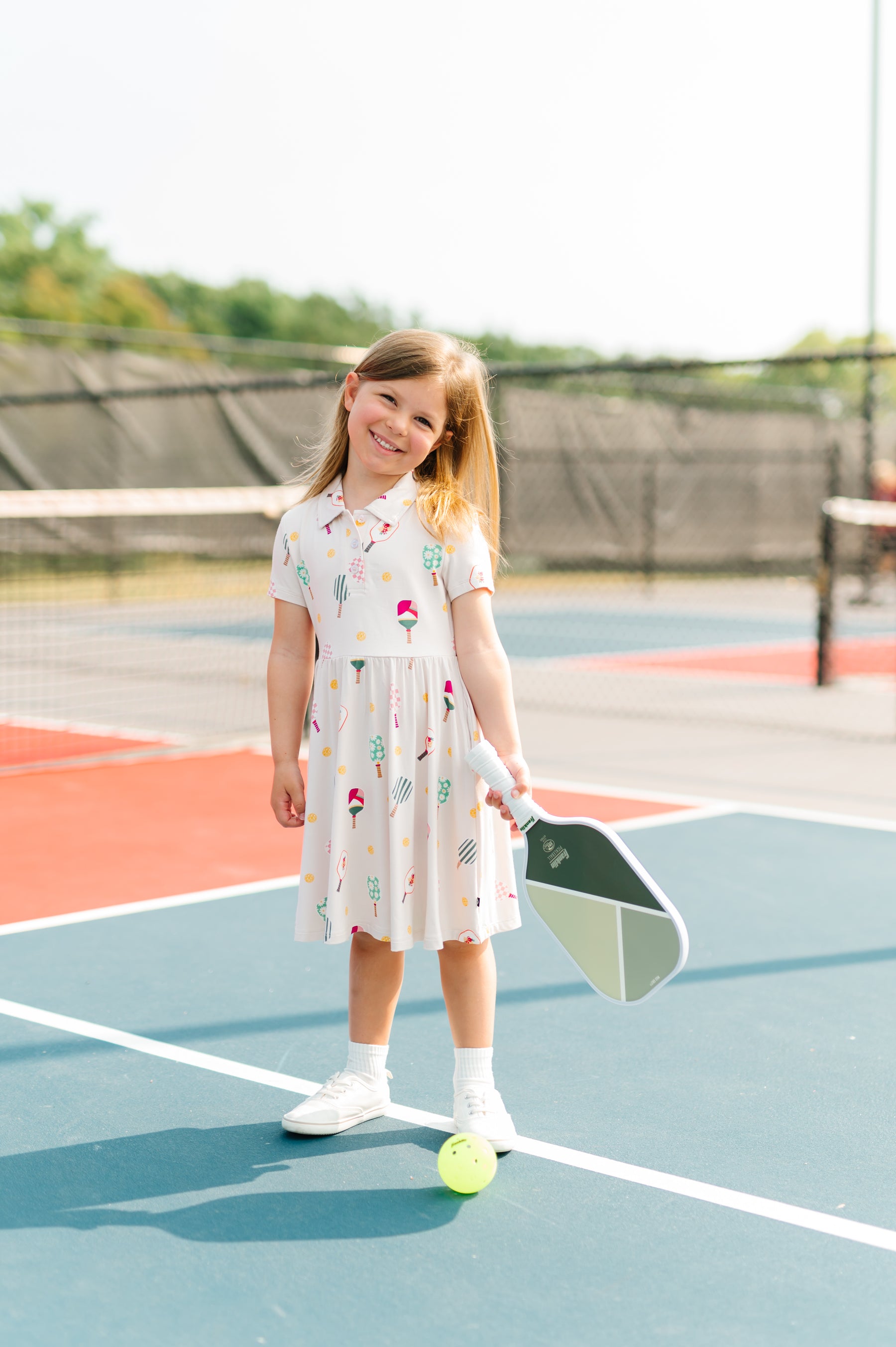 Girl smiling on pickleball court wearing Polo Dress in Pickleball print