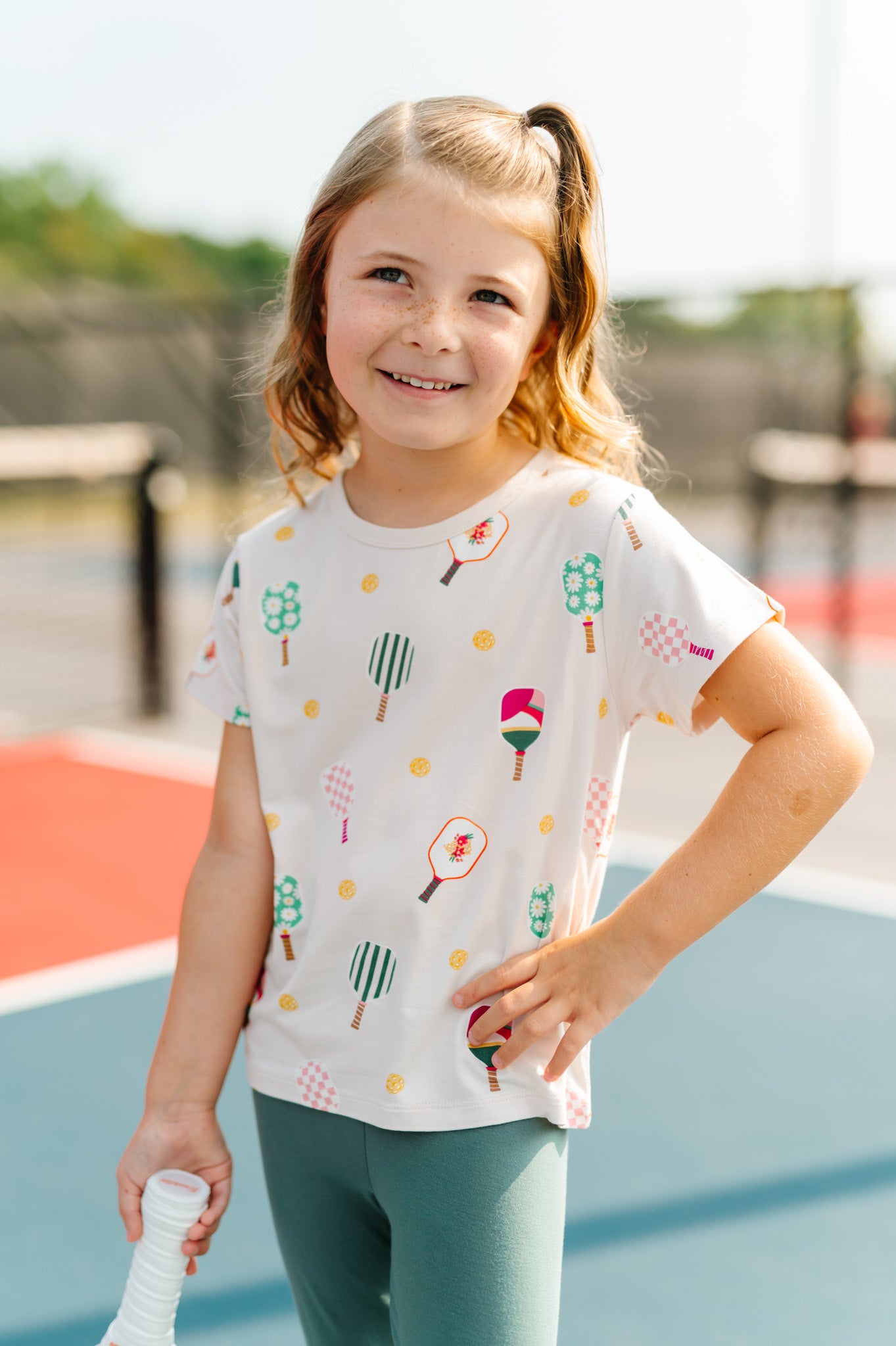 Girl wearing Toddler Basic Tee in Pickleball print over a green leggings 