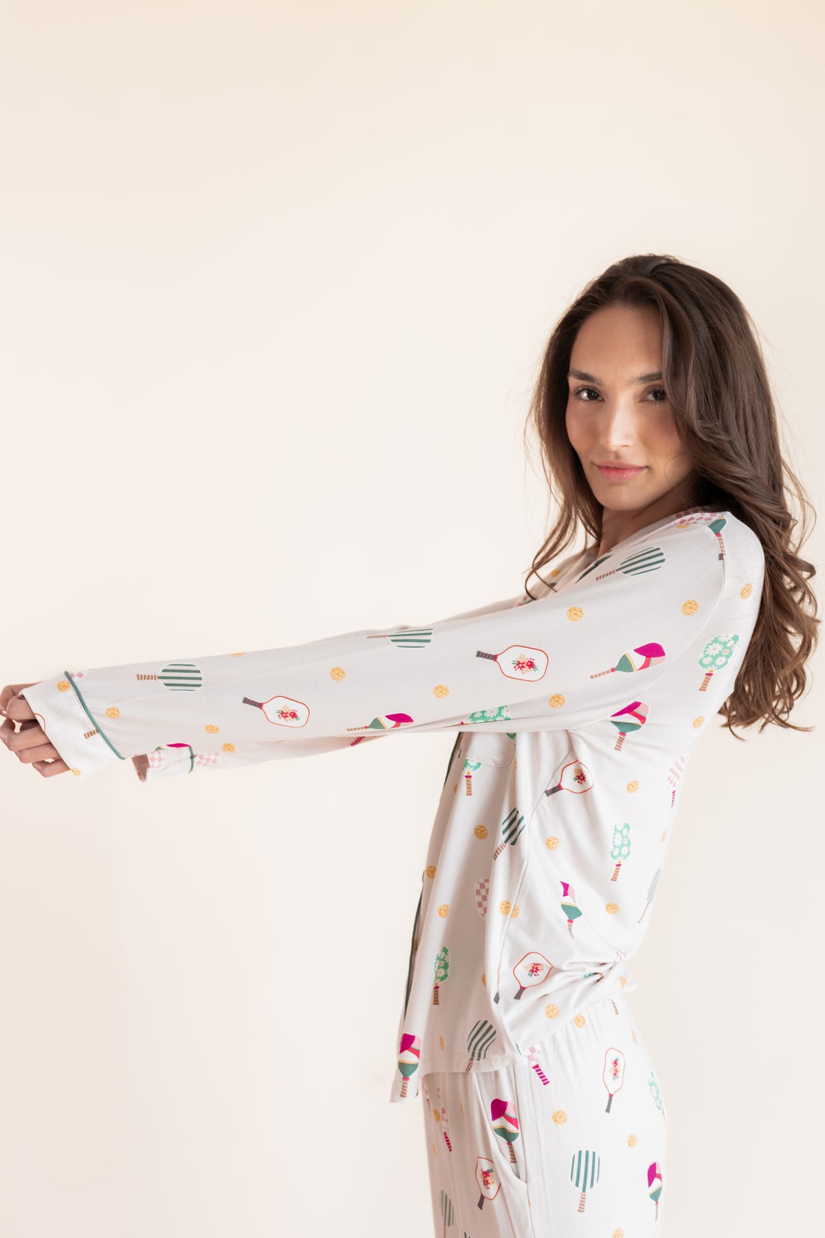 A woman modeling a long-sleeve white pajama set with a colorful pickleball  print, posed against a solid light beige background.