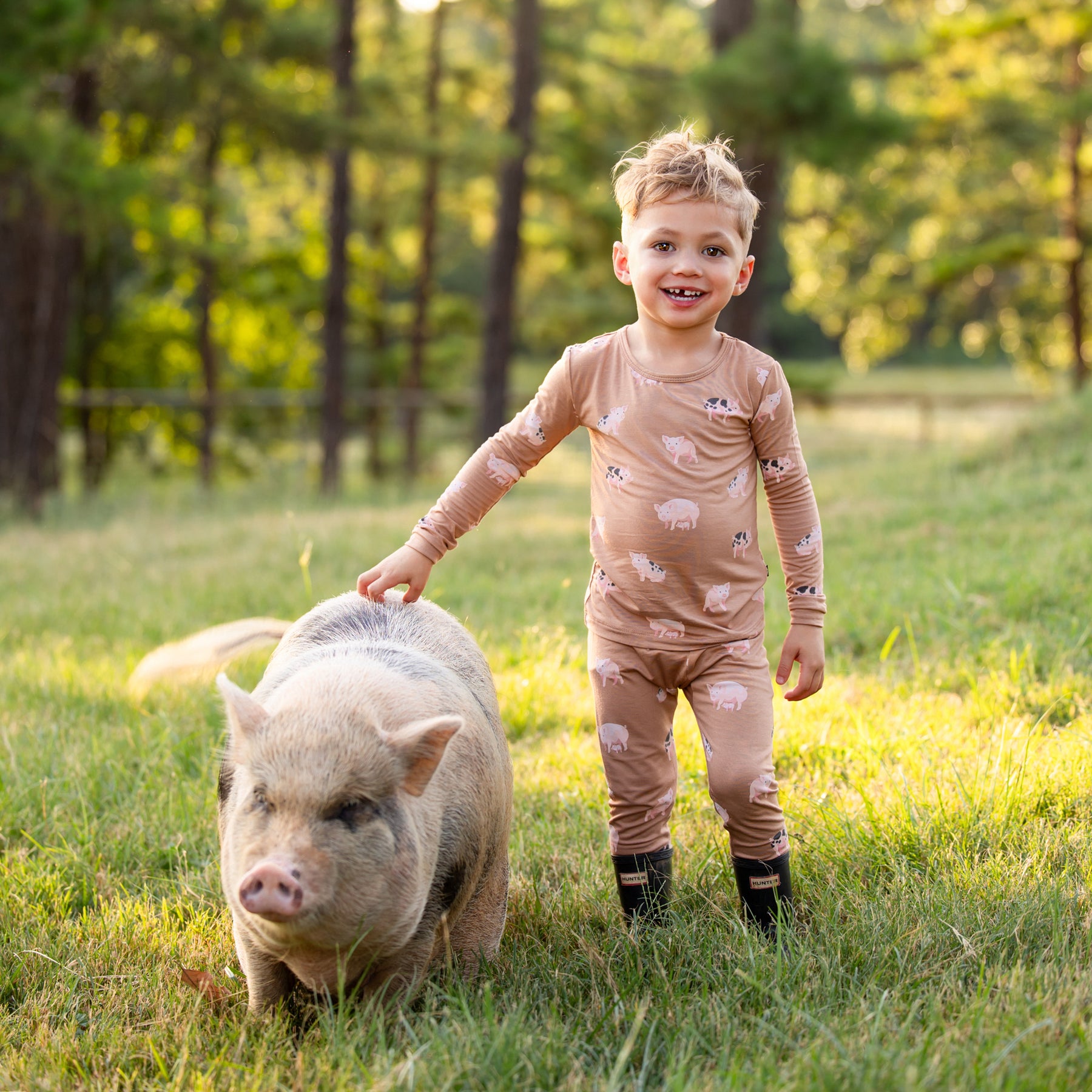 Young boy standing in the field with his pet big wearing the Long Sleeve Pajamas in Pig and Hunter Rainboots