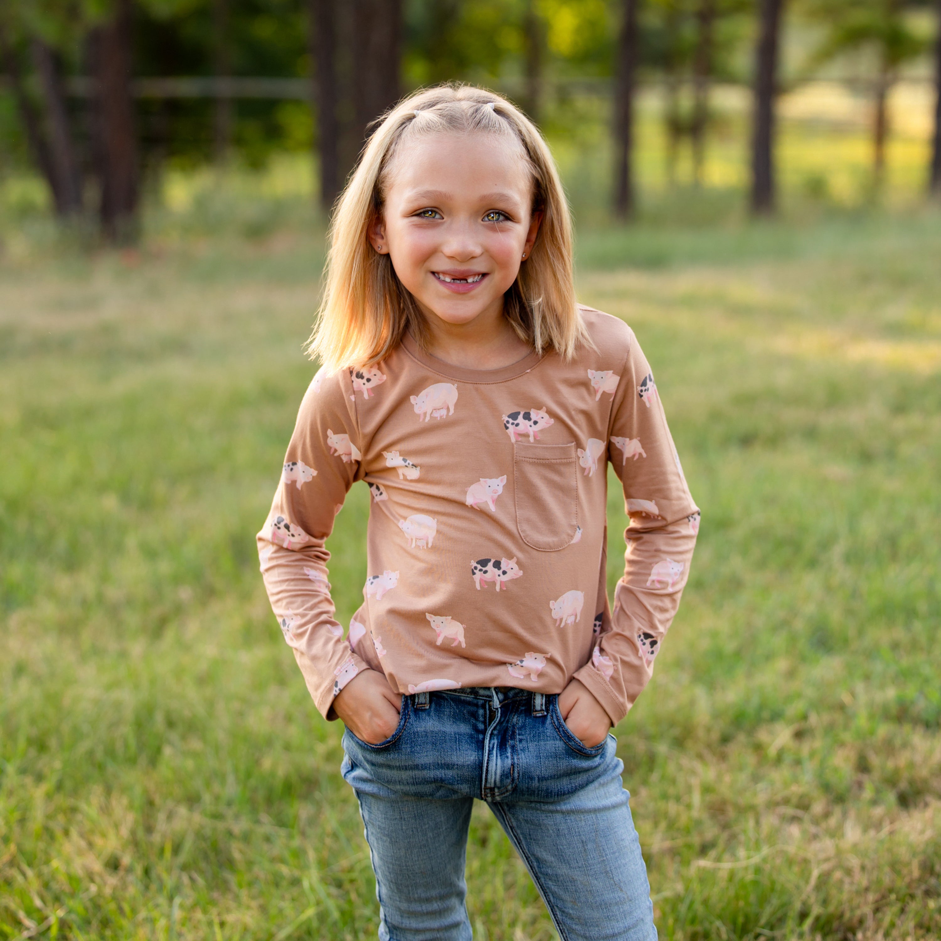 Girls standing in a field with her hands in her jean pockets wearing the Long Sleeve Toddler Crew Neck Tee in Pig