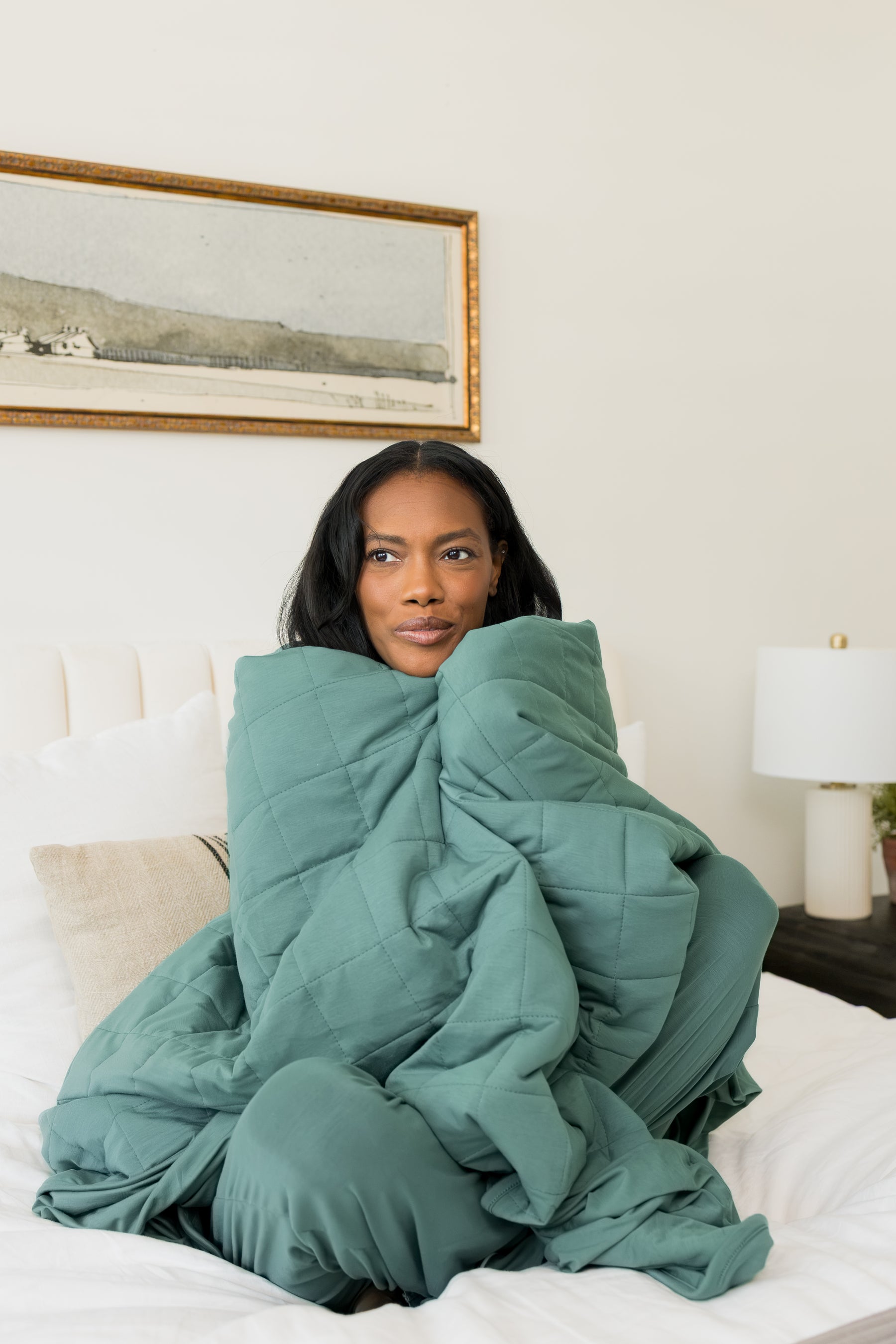 Model sitting on bed wrapped in Adult Quilted Blanket in Pine 2.5