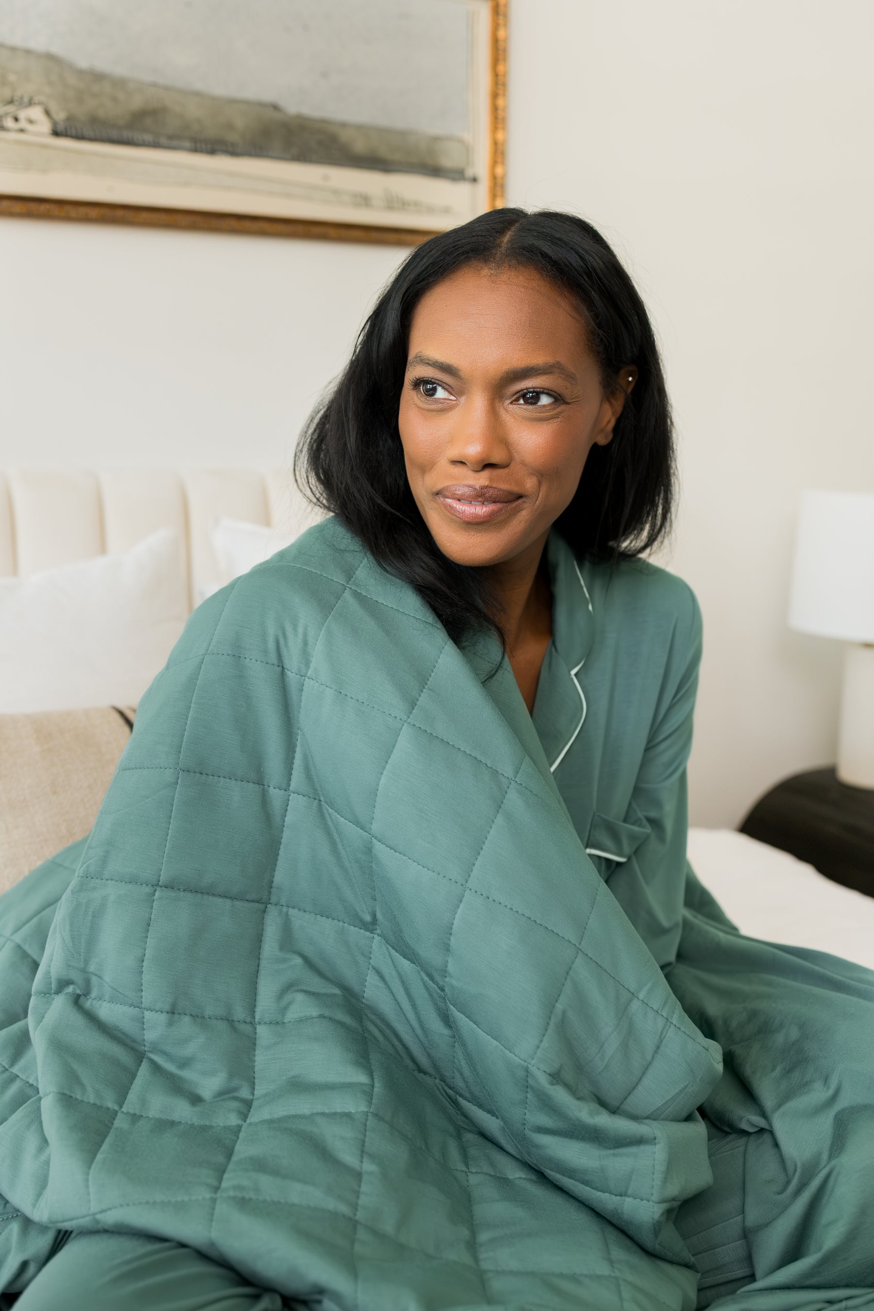 Model sitting on bed wrapped in Adult Quilted Blanket in Pine 2.5 wearing similar color women's long sleeve pajama set