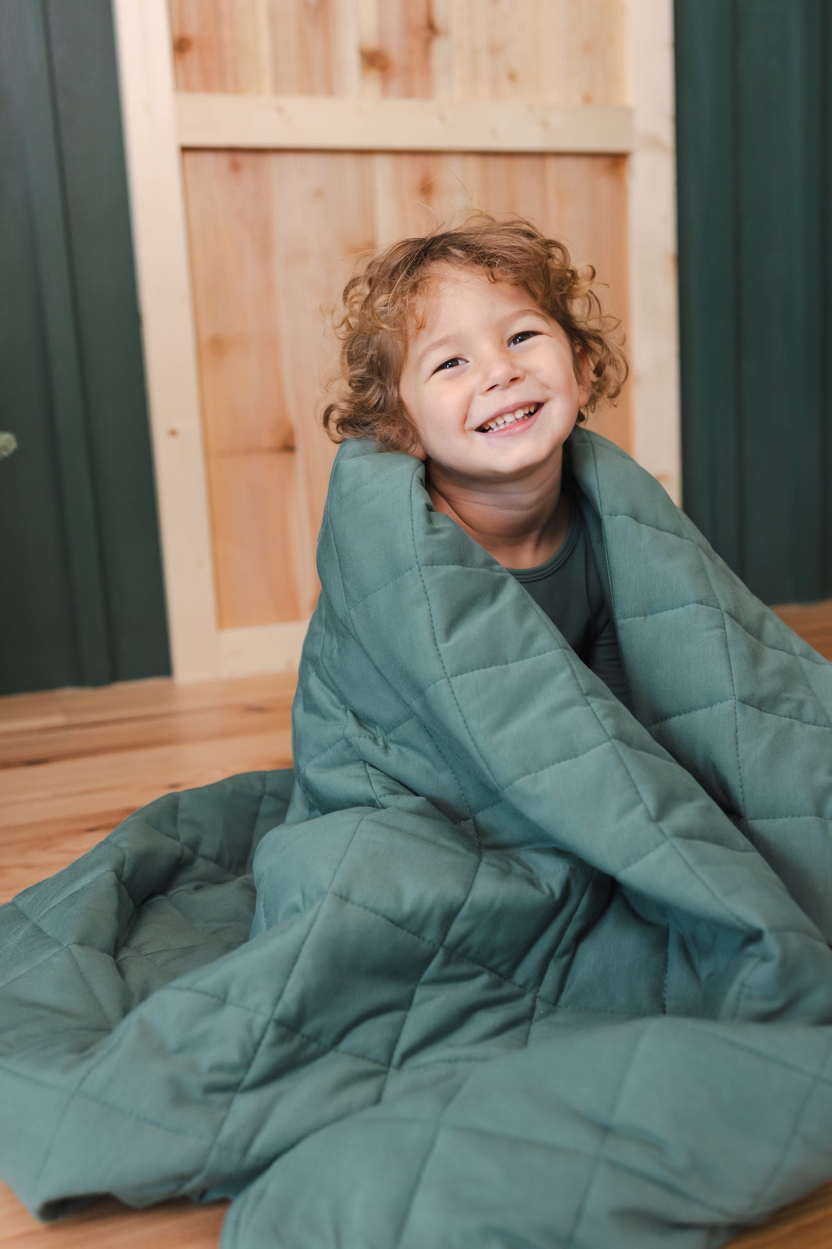 Toddler sitting on floor while wrapped in Youth Blanket in Pine 2.5